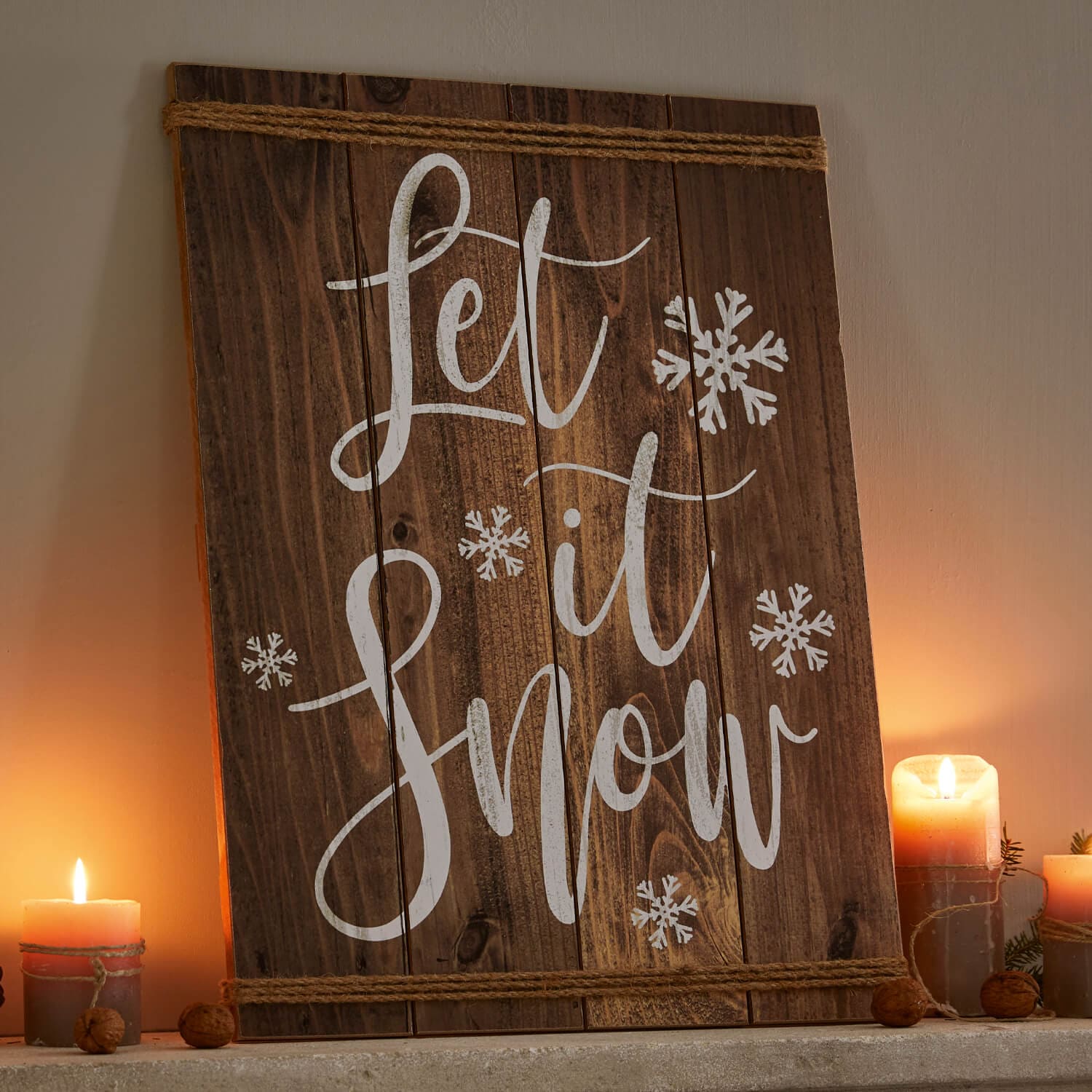 Holz-Wanddeko mit Schriftzug Let it Snow und weißen Schneeflocken, umgeben von brennenden Kerzen