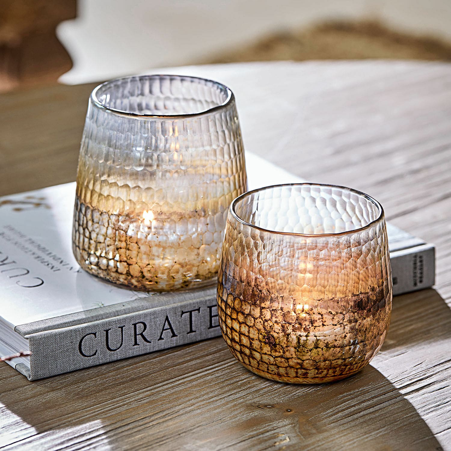 Windlicht 2er Set Agnús Zwei strukturierte Glas-Teelichthalter in Braun auf Holztisch neben einem Buch
