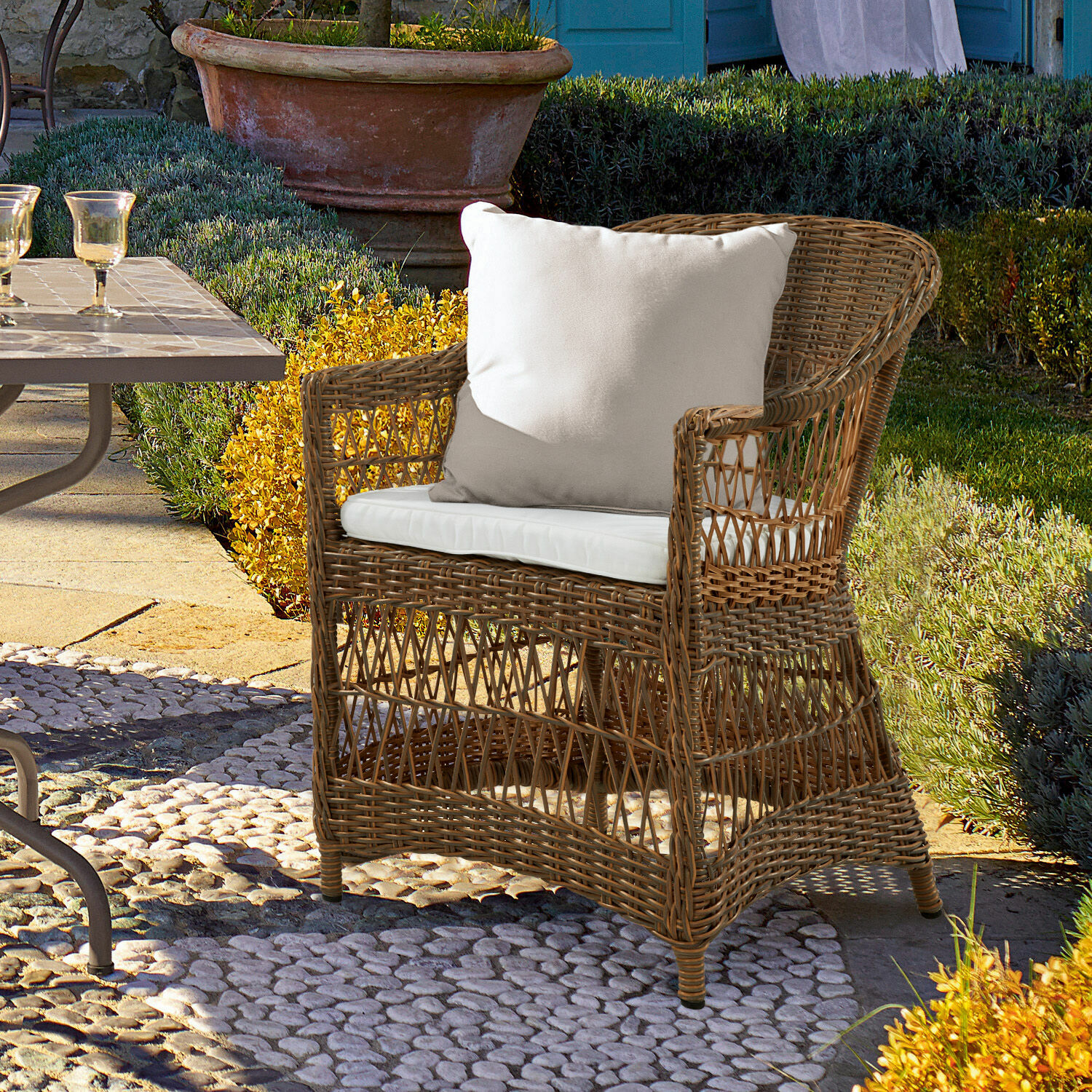 Sessel Garden Grove Rattansessel mit weißem Kissen auf Steinboden im Garten für Outdoor-Möbel