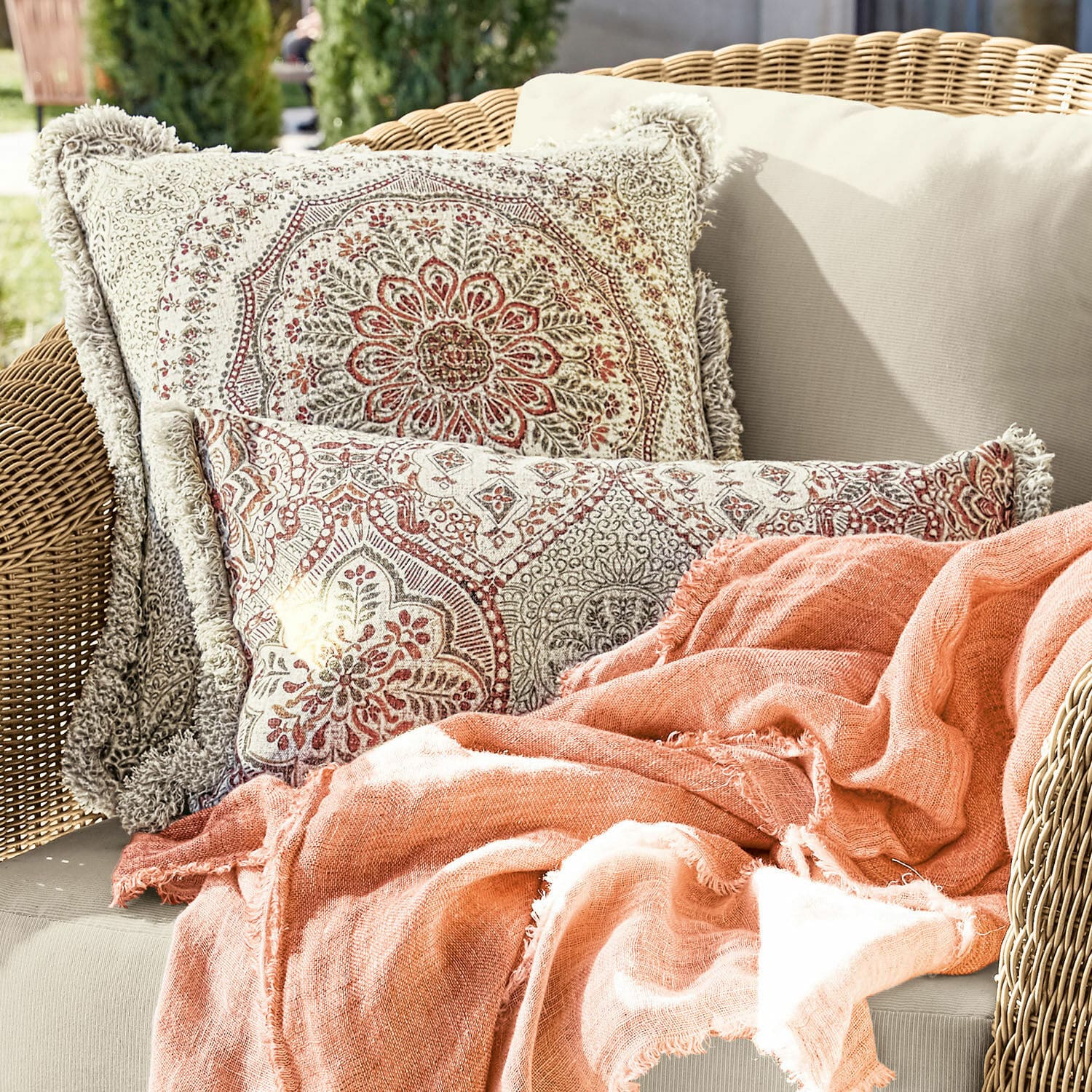 Kissenhülle 2er Set Margret Beidseitige Baumwollkissen mit beigem und rotem Muster und orangefarbene Decke auf Rattansofa