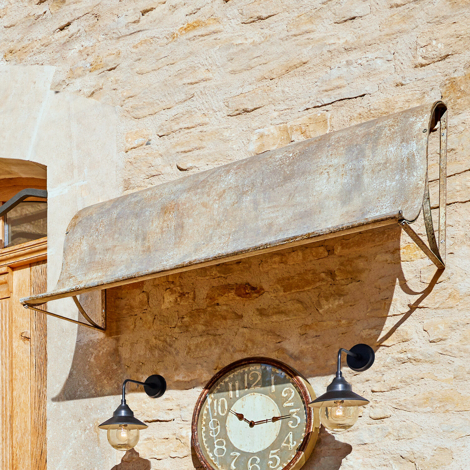Vordach Lison Verwittertes graues Metallvordach an Steinmauer mit antiker Uhr und schwarzen Lampen