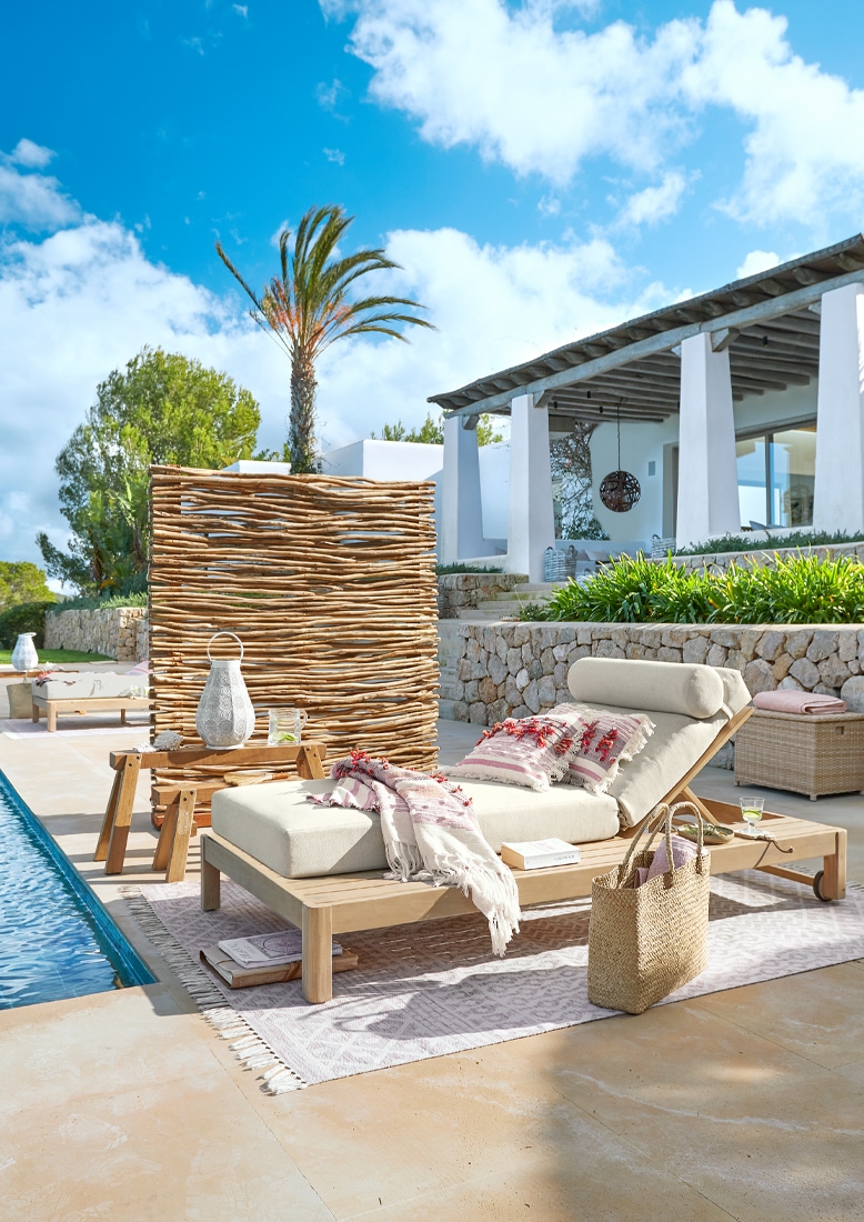 Liegestuhl aus hellem Holz mit cremefarbenem Polster und dekorativer Decke am Pool auf der Terrasse