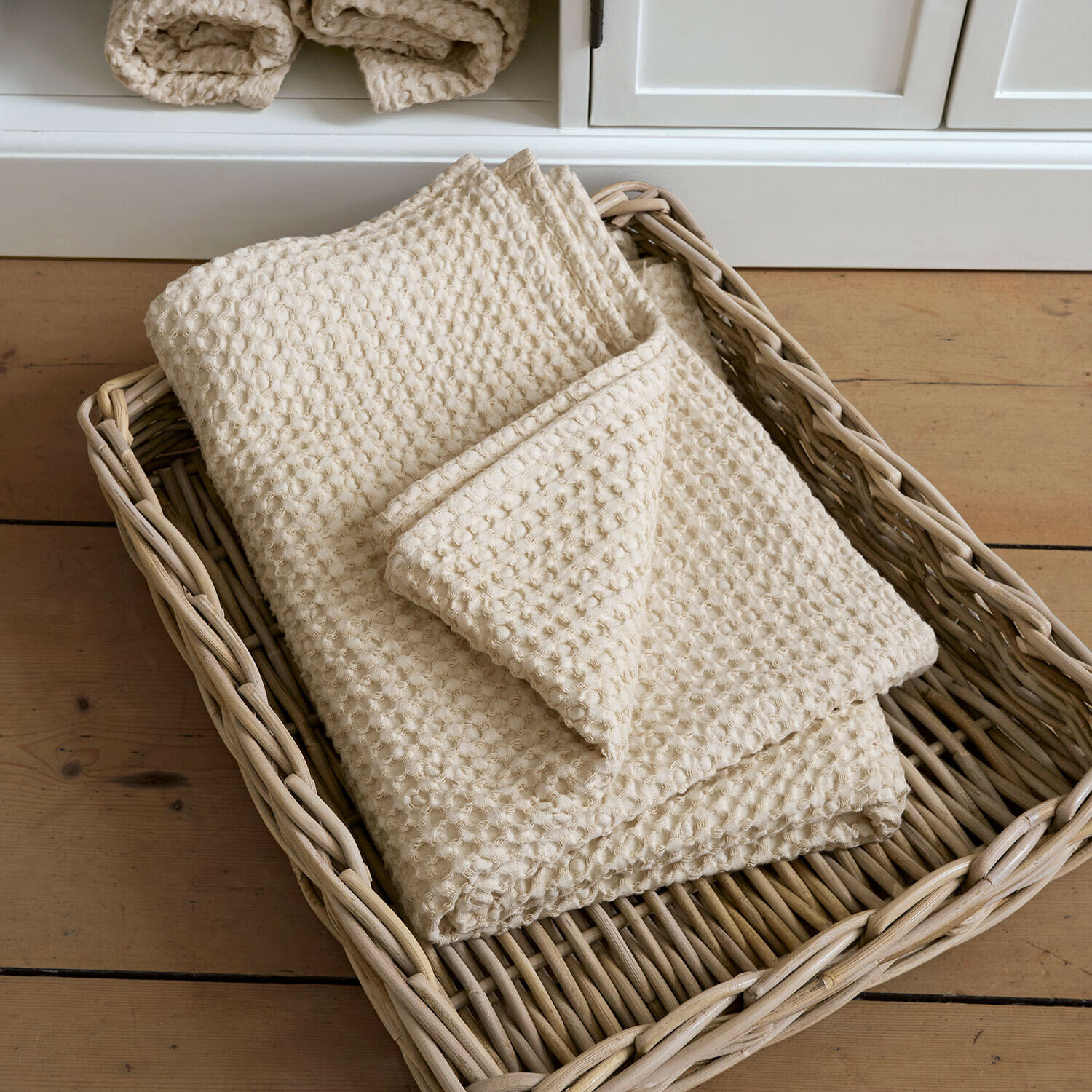 Badetuch Maralei Cremefarbene Baumwolldecke mit Waffelstruktur in einem Korb aus Rattan auf Holzboden