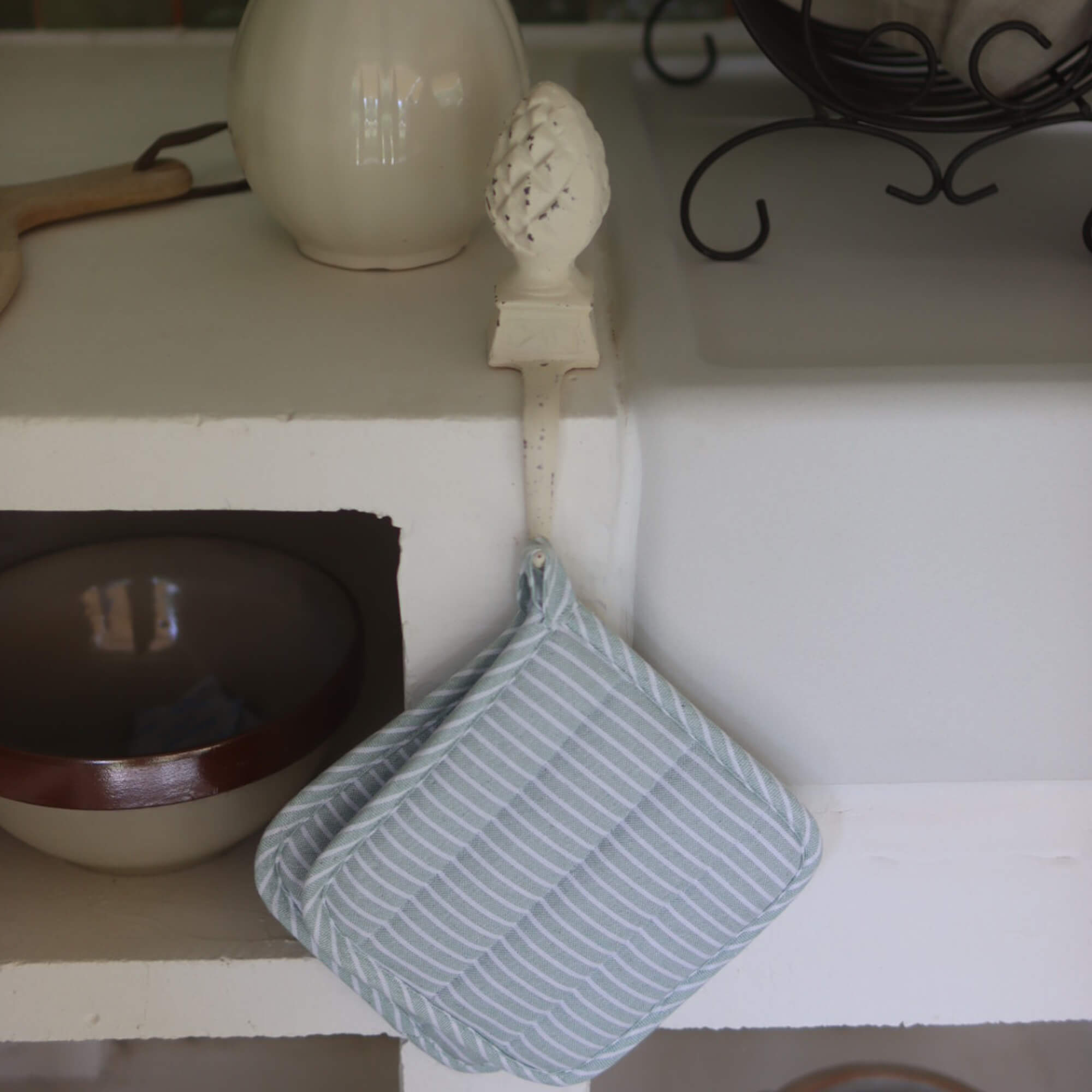 Mintgrün-weiß gestreifter Baumwoll-Topflappen an Metallhaken in der Küche hängend