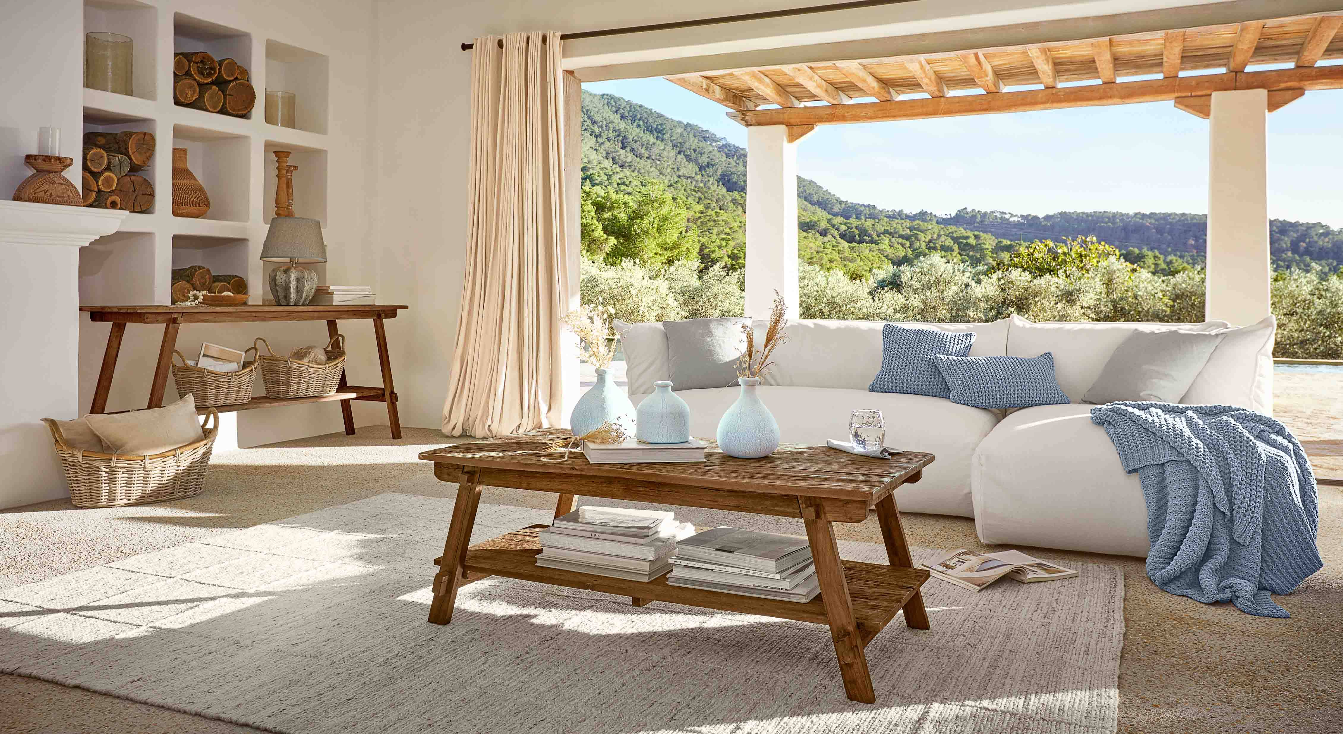 Gemütliches Wohnzimmer mit rustikalem Holztisch und weißem Sofa mit blauer Decke und Kissen