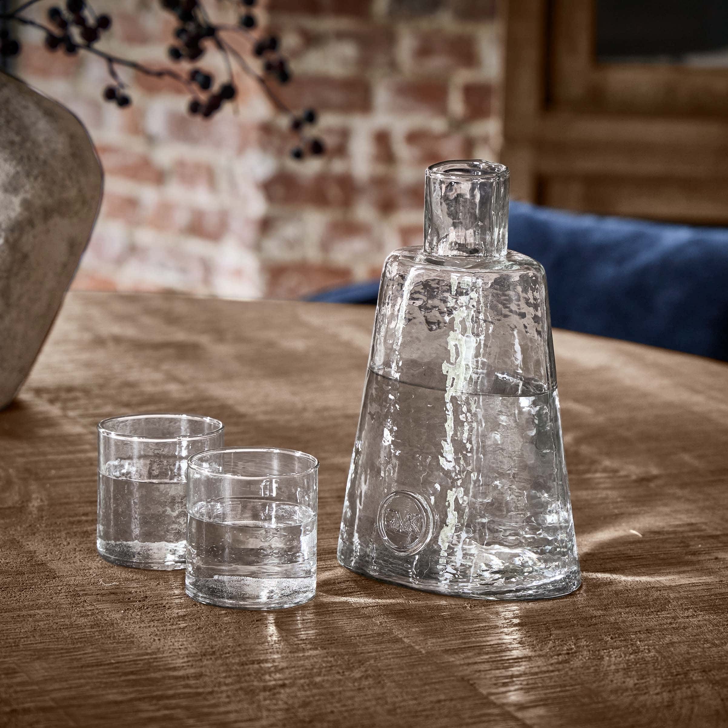 Transparente Glas-Karaffe mit zwei Gläsern auf Holztisch in rustikalem Ambiente