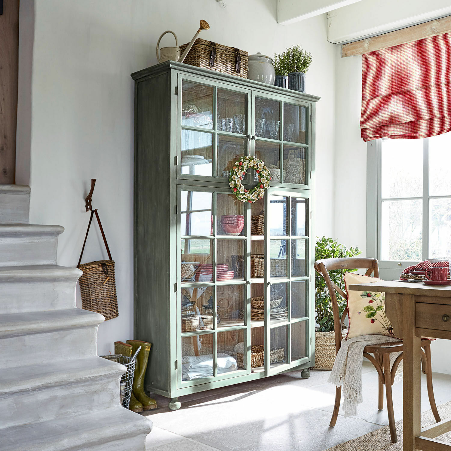 Grüner Holzvitrinenschrank mit Glastüren in hellem Raum mit natürlicher Dekoration