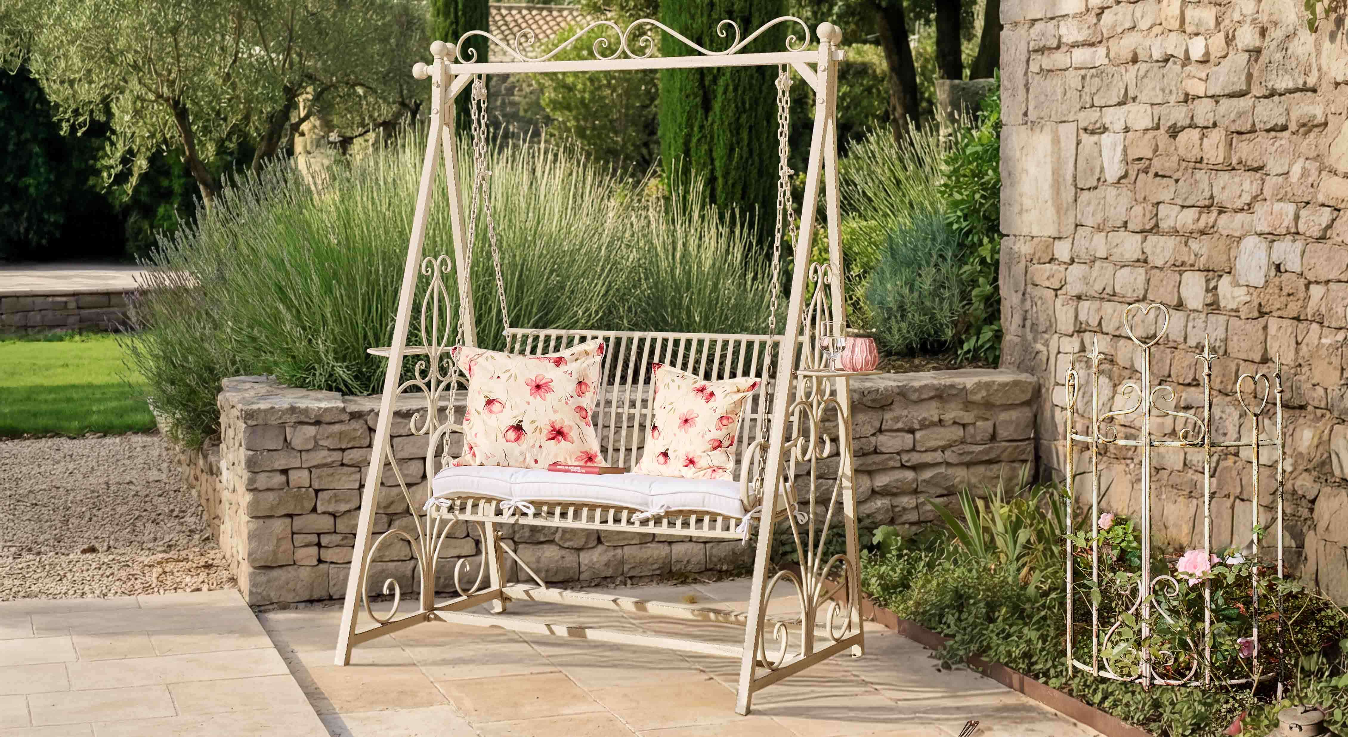 Metall-Gartenschaukel in Creme mit floral gemusterten Kissen auf Naturstein-Terrasse