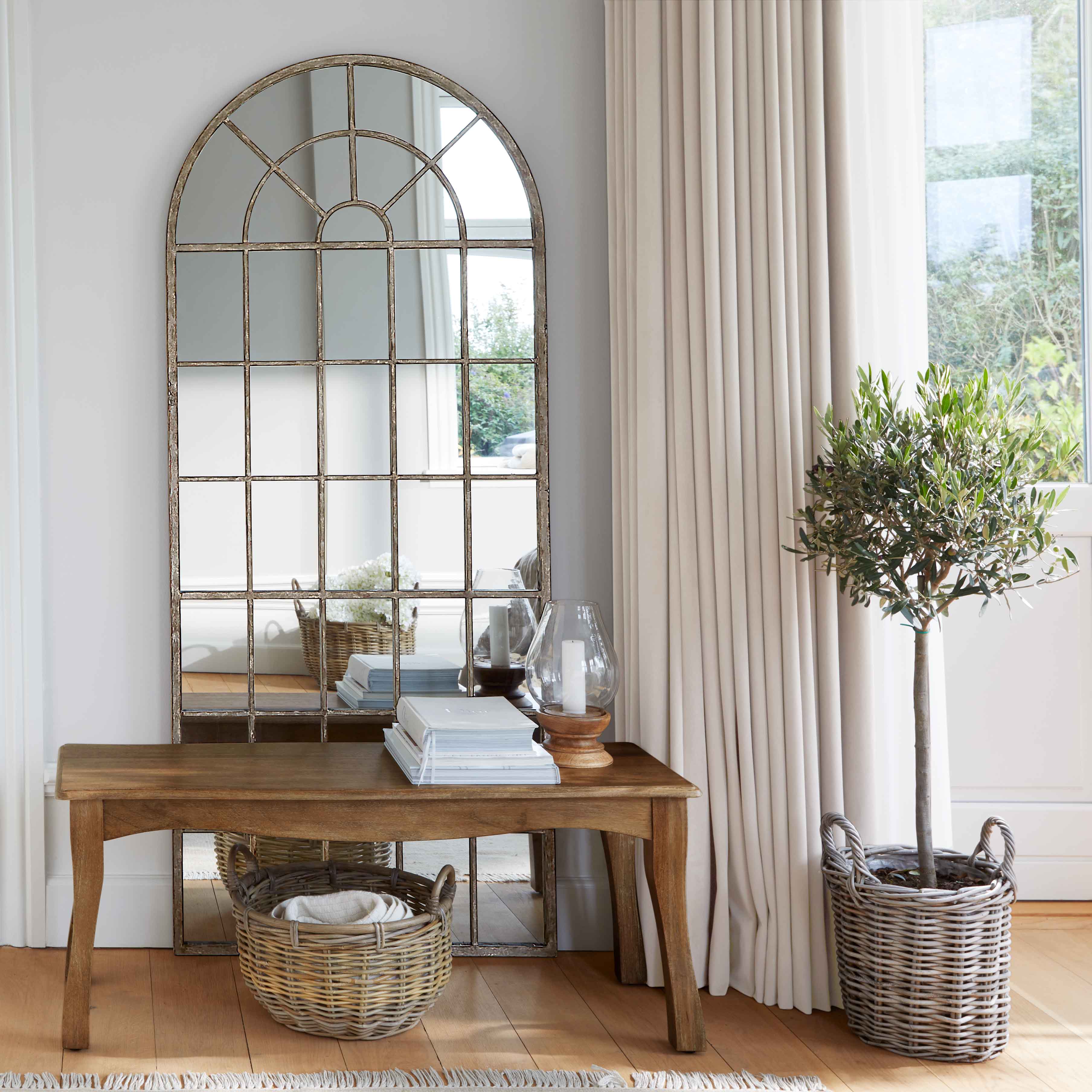 Holztisch mit Metallrahmen-Spiegel und Korb aus Weide in hellem Raum mit Vorhängen