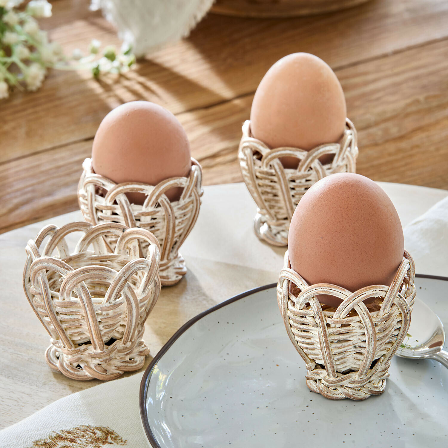 Vier weiße, antik wirkende Eierbecher aus geflochtenem Korbmaterial auf Holztisch