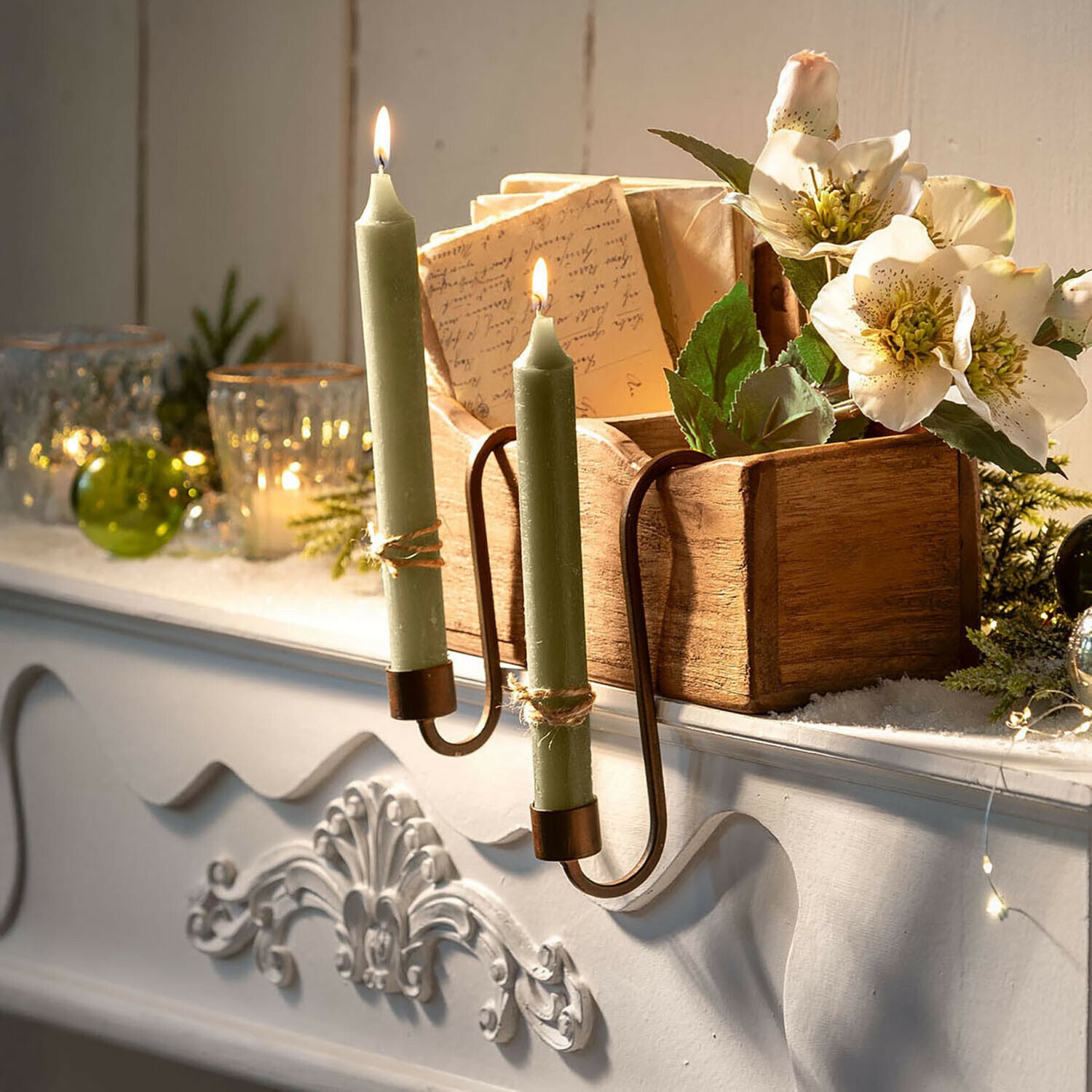 Kerzenhalter 2er Set Fioriva Grüne Kerzen im Metallkerzenhalter an weißem Kamin mit Holzkiste und Blumen dekoriert