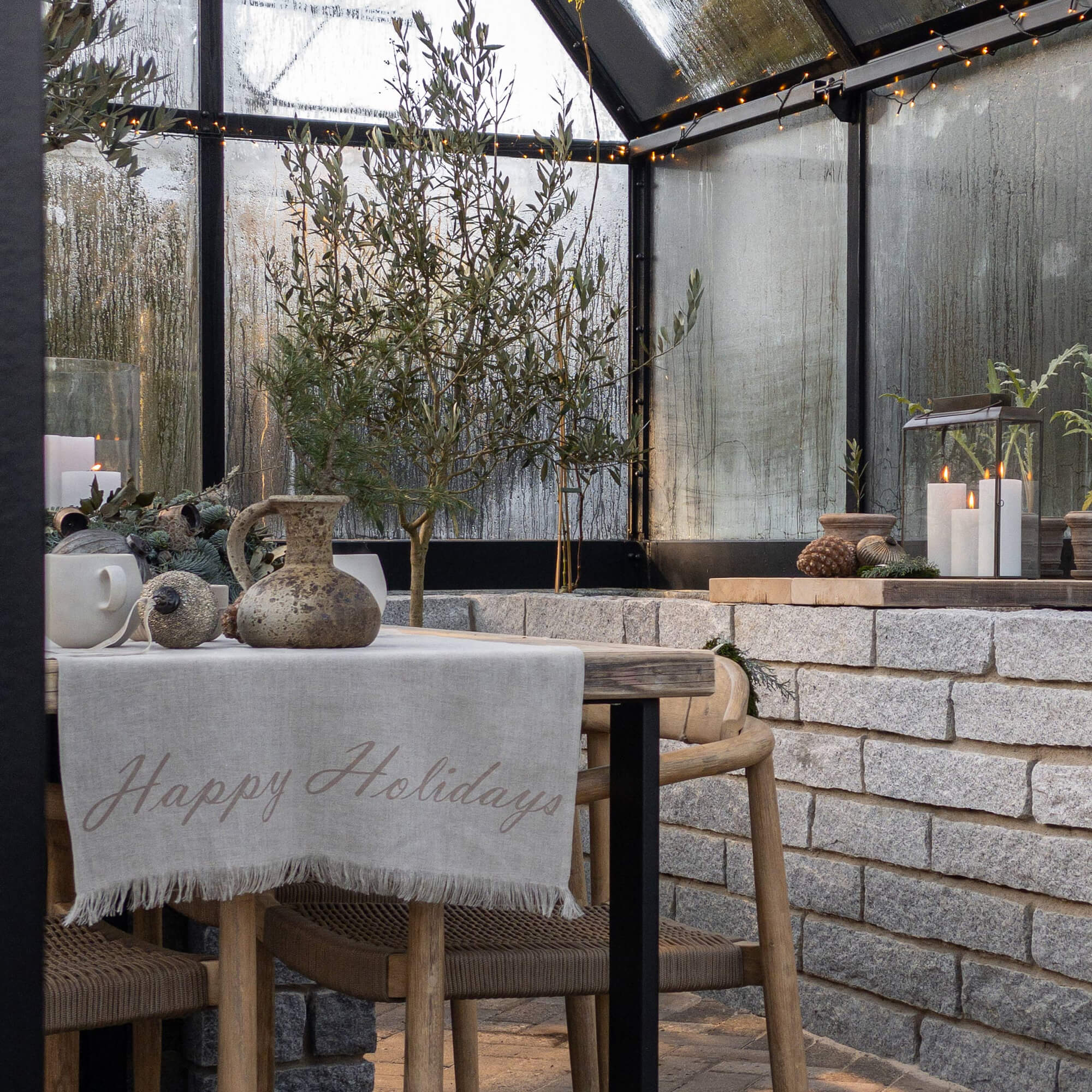 Gemütliche Sitzecke mit Holztisch, Leinentischdecke und Weihnachtsdekoration im Gewächshaus