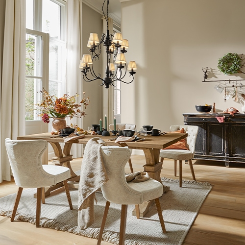 Esszimmer mit massivem Holztisch, cremefarbenen Polsterstühlen, Blumenarrangement und schwarzem Kronleuchter