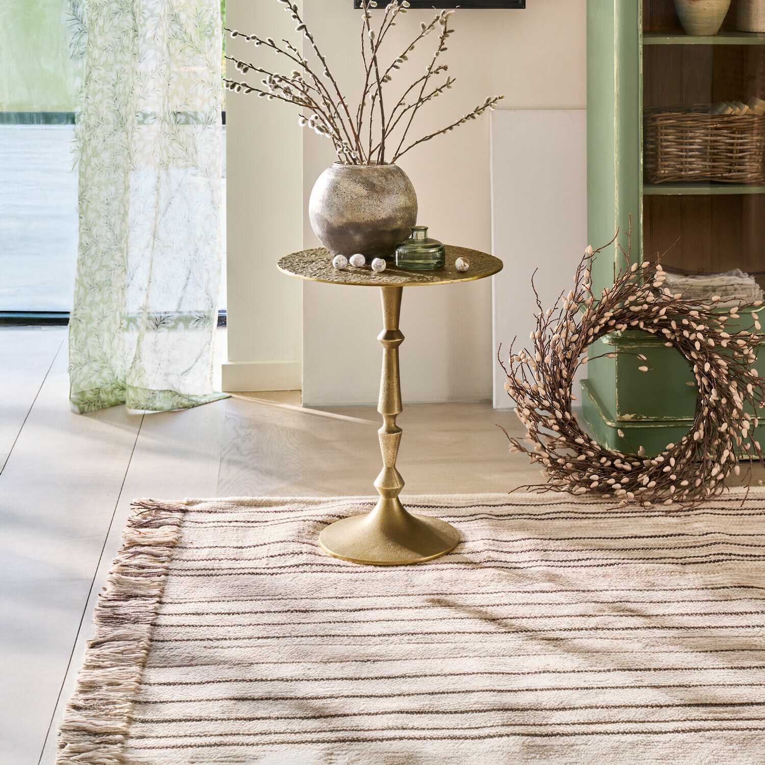 Goldener Metall-Beistelltisch mit dekorativer Vase und Zweigen in hellem, gemütlichem Raum mit Teppich