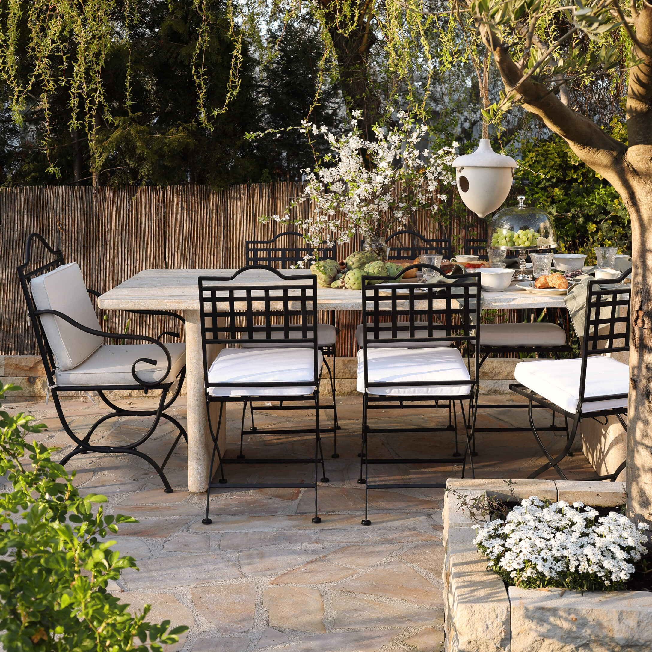Gartenmöbel-Set mit schwarzen Metallstühlen und hellem Steintisch auf sonniger Terrasse