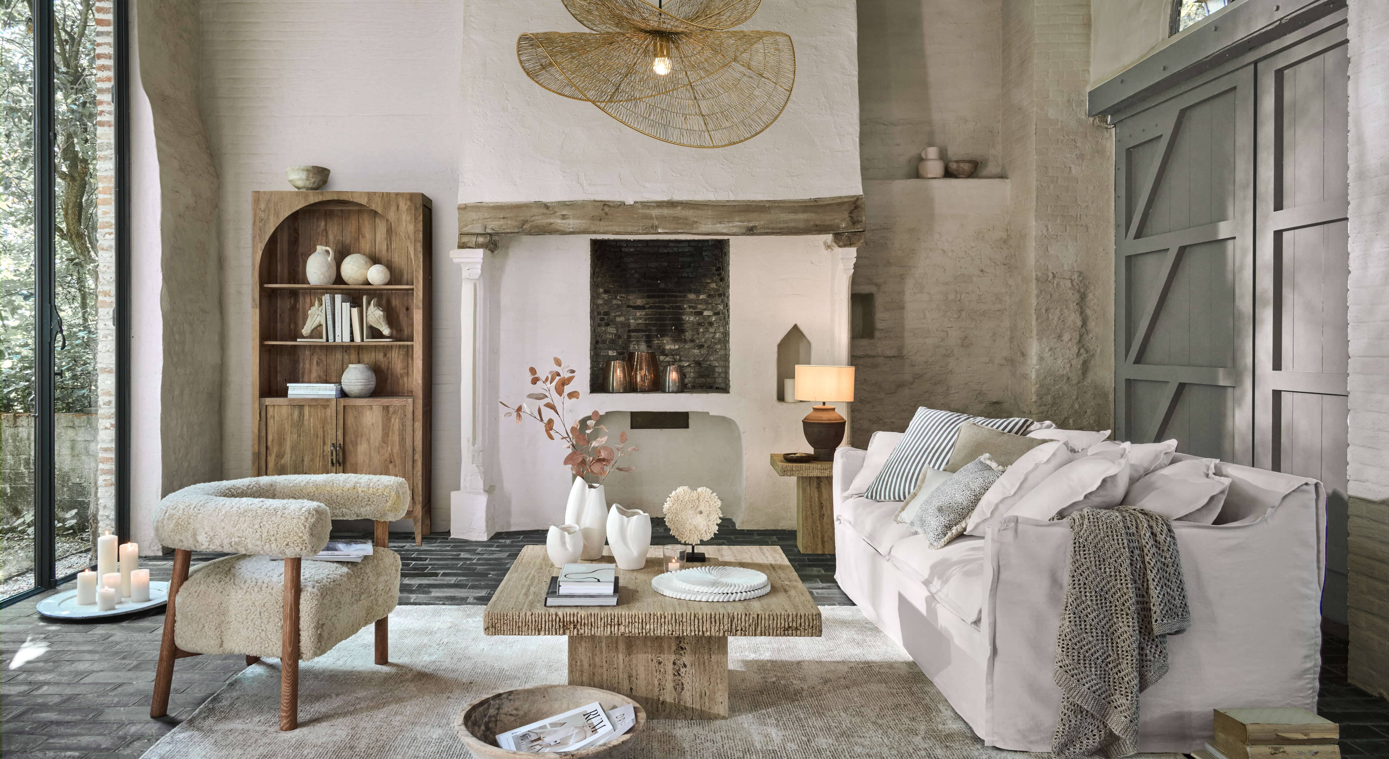 Gemütliches Wohnzimmer mit weißem Sofa, beigem Stoffsessel und Holzcouchtisch auf hellem Teppich