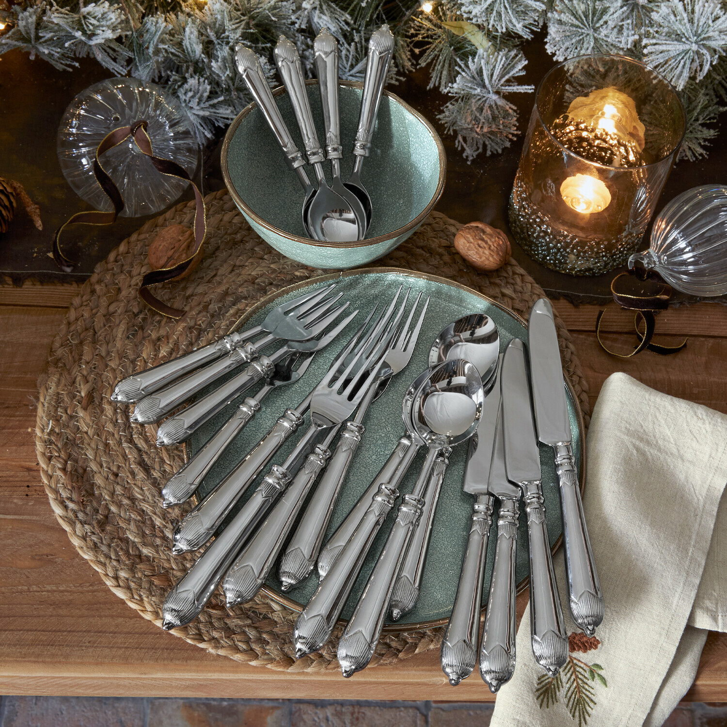 Set silberner Edelstahlbestecke auf grünem Teller und Schale mit weihnachtlicher Dekoration