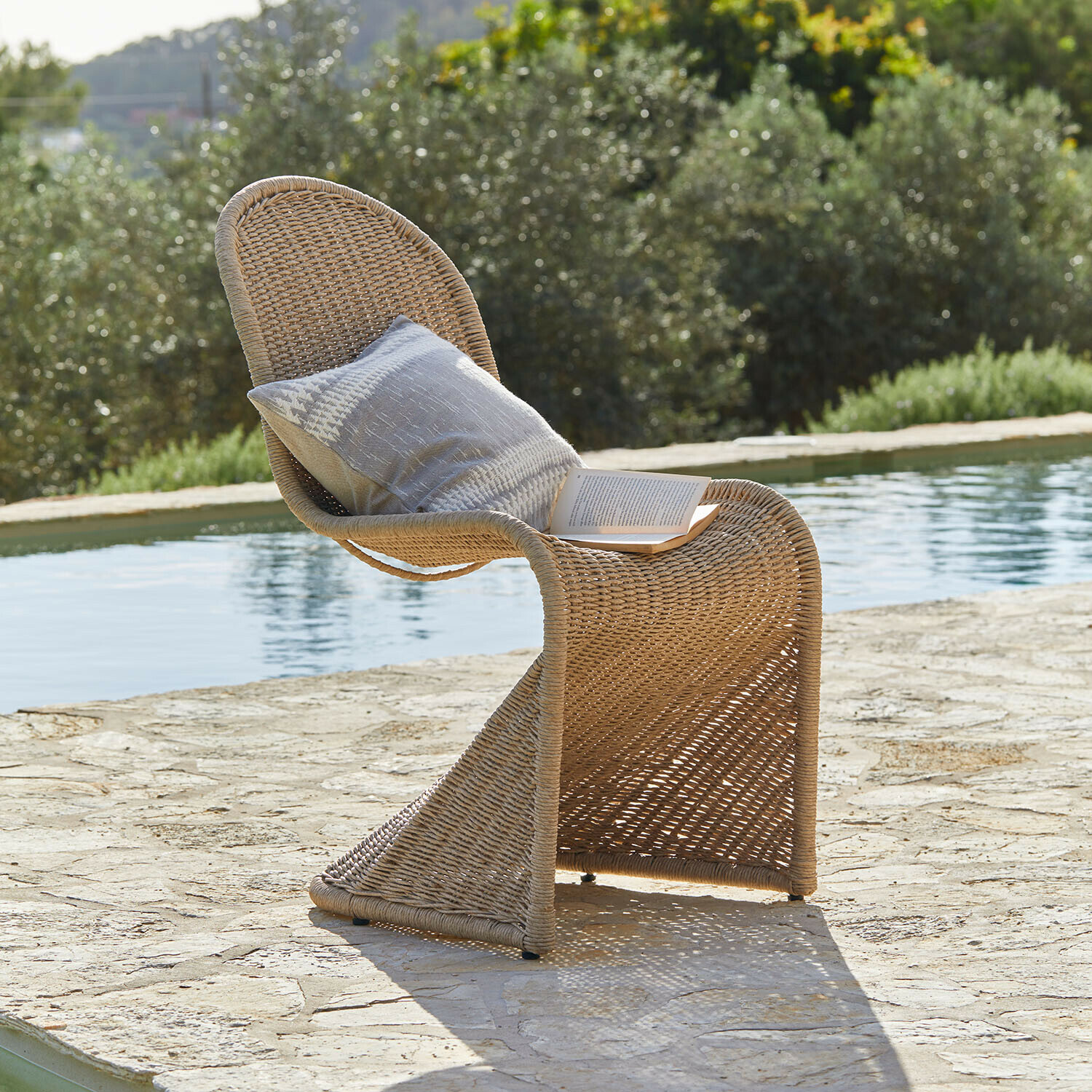 Stuhl Melari Gartenstuhl aus natürlichem Flechtmaterial mit Kissen und Buch am Poolrand