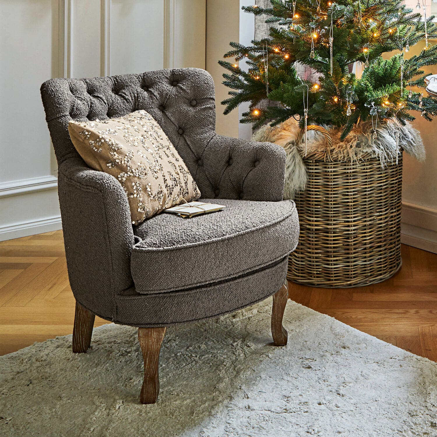 Sessel Calgary Grau gepolsterter Sessel mit Holzbeinen auf hellem Teppich neben geschmücktem Weihnachtsbaum