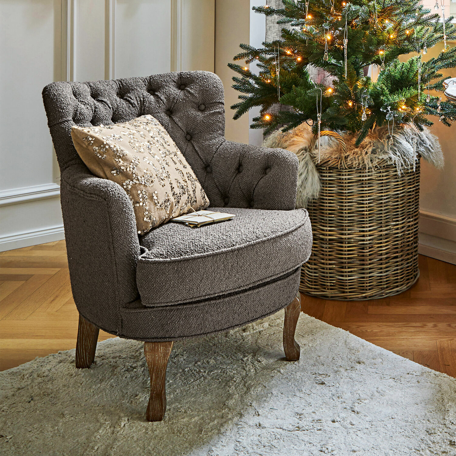 Sessel Calgary Grau gepolsterter Sessel mit Holzbeinen auf hellem Teppich neben geschmücktem Weihnachtsbaum