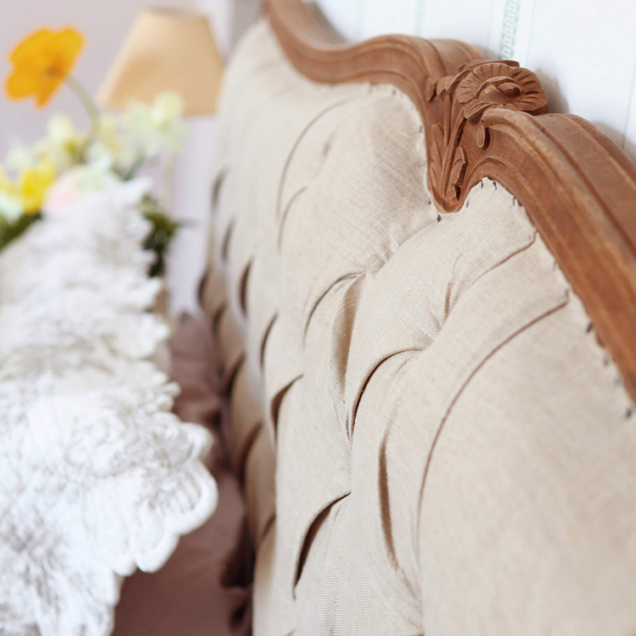 Beige gepolsterte Rückenlehne mit geschnitztem Holzrahmen und dekorativem Kissen im Hintergrund