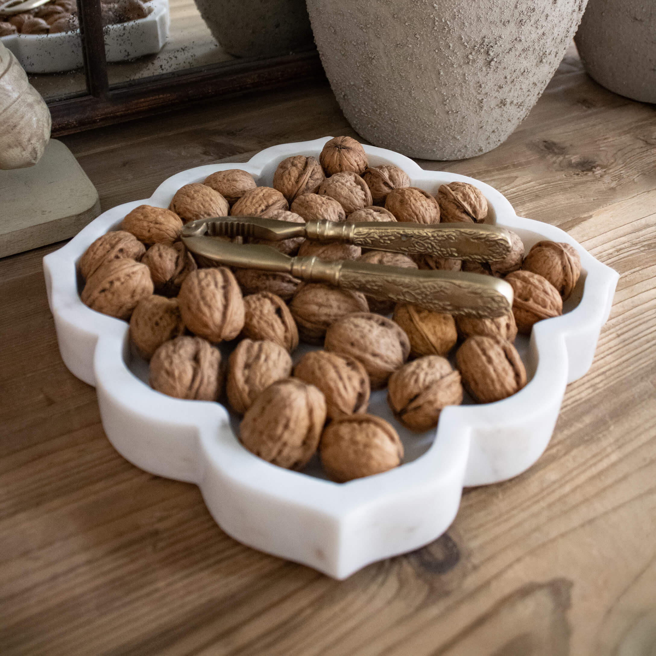 Weiße Marmorplatte mit Walnüssen und goldenem Nussknacker auf Holztisch