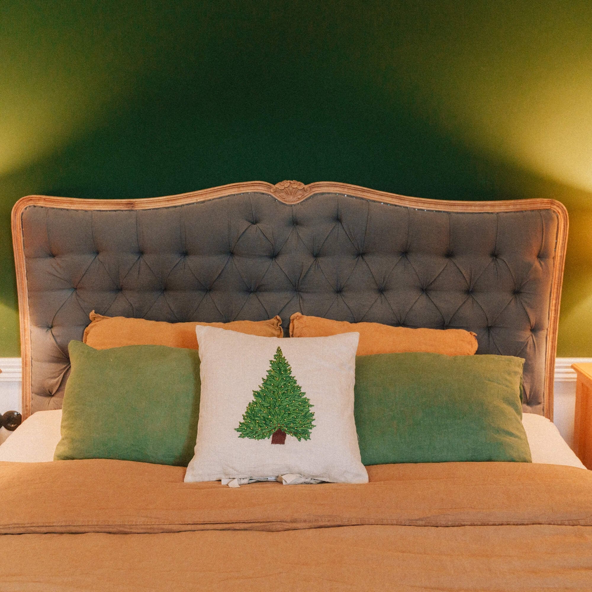 Schlafzimmer mit grauem, gepolstertem Kopfteil und grünen sowie orangefarbenen Kissen, weihnachtliche Dekoration