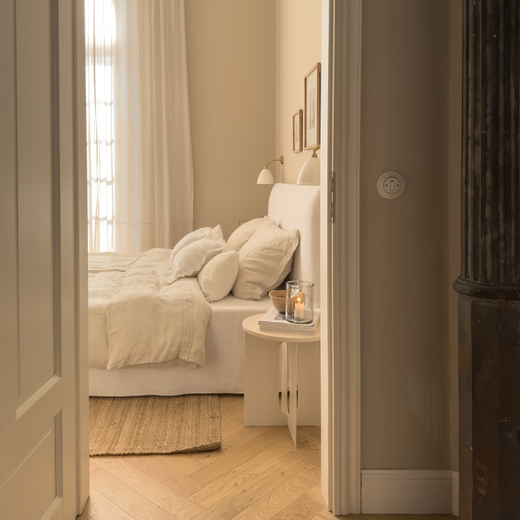 Gemütliches Schlafzimmer in hellen Beigetönen mit Bett und Naturteppich auf hellem Holzboden