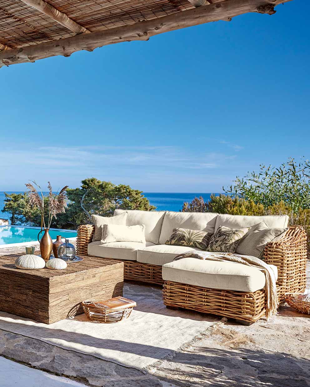 Rattan-Gartenmöbel-Set mit cremefarbenen Polstern auf Terrasse mit Meer- und Poolblick