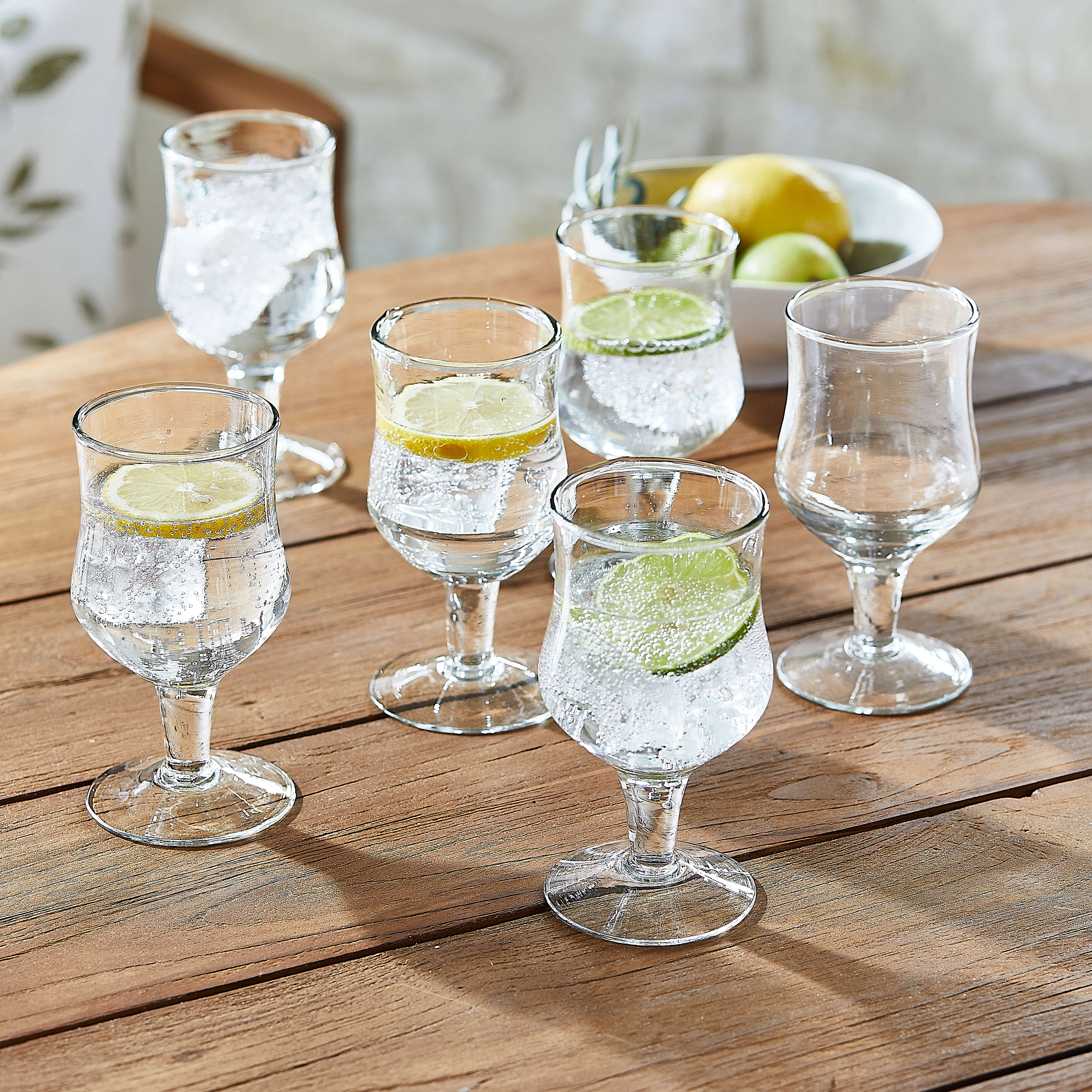 Sechsteiliges Set transparenter Gläser mit Wasser, Zitronen- und Limettenscheiben auf Holztisch