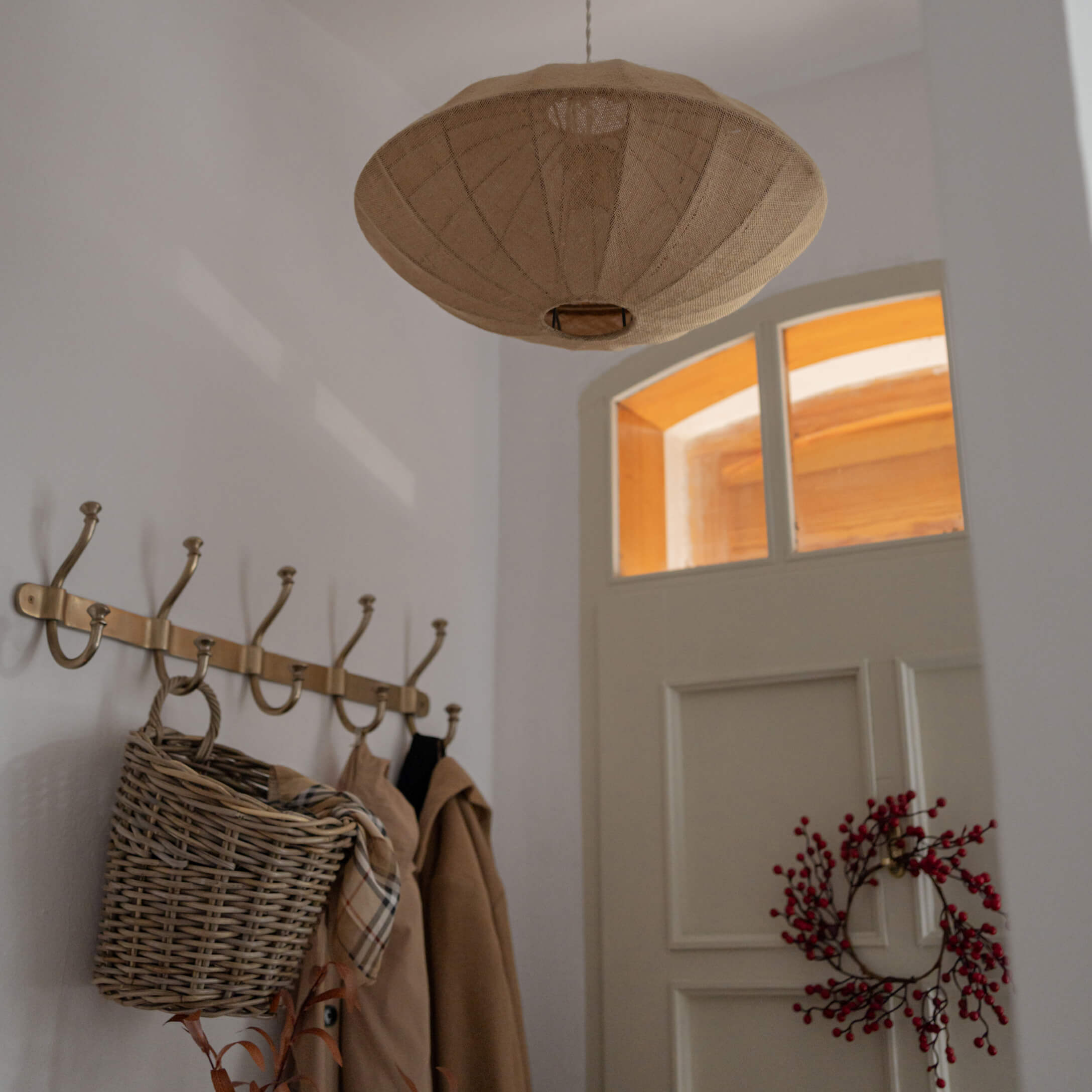 Beige Stoff-Hängelampe in schirmförmigem Design über Garderobe mit Korb und roten Beeren an weißer Tür