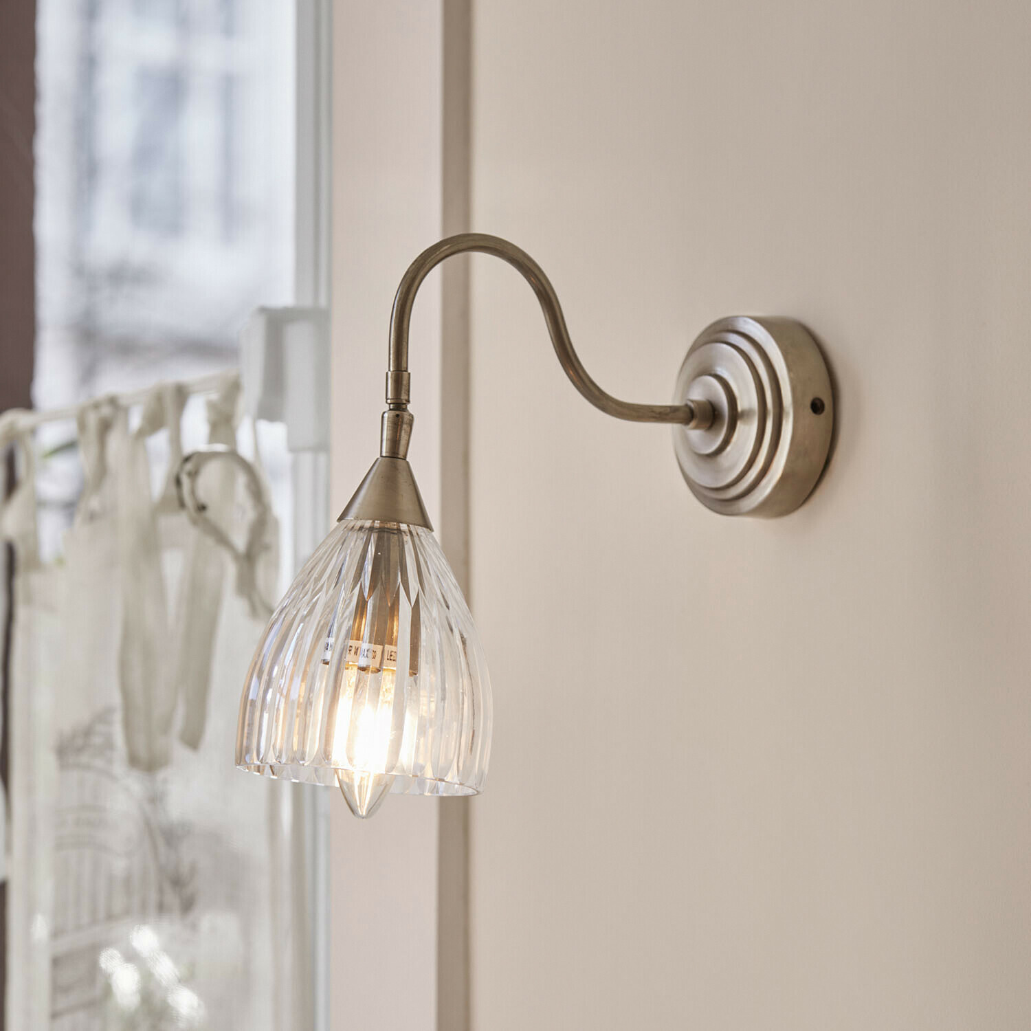 Wandlampe Niamhs Wandleuchte mit klarem Glaslampenschirm und gebogenem Metallarm in antik-silberner Farbe