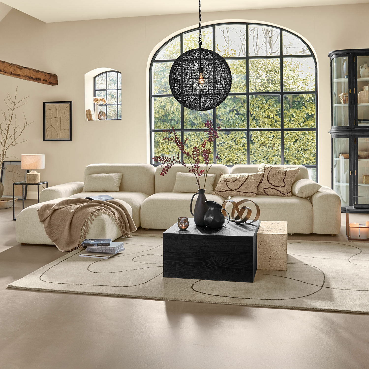 Sofa Marnivelle Beige Ecksofa mit weichen Kissen und schwarzem Couchtisch in modernem Wohnzimmer mit großen Fenstern