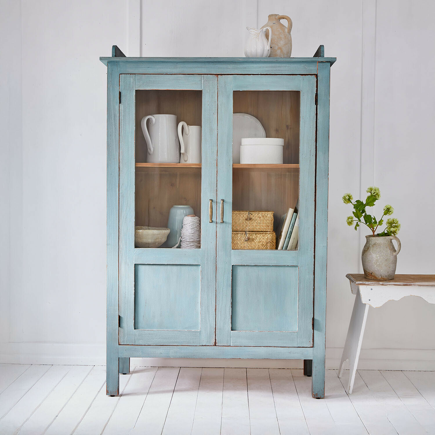 Blauer Holzschrank mit Glastüren und Vintage-Keramikdekorationen in hellem Raum