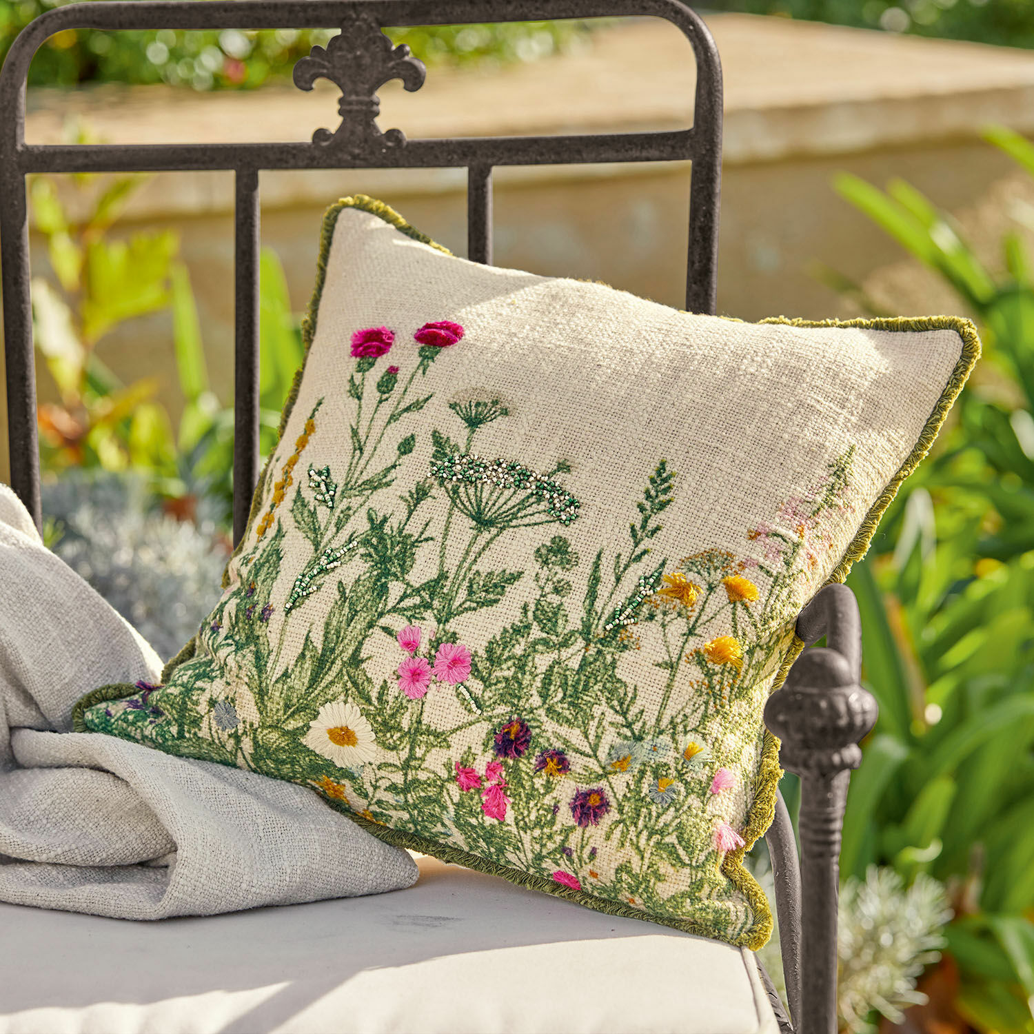 Kissenhülle Aranno Beige Leinenkissen mit bunter Blumenstickerei und grünem Rand auf einem Metall-Gartenstuhl