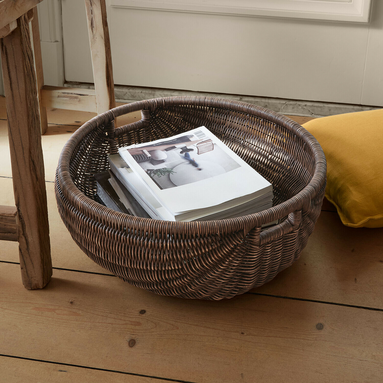 Korb Veltris Runder Korb aus dunklem Rattan mit Griffen, gefüllt mit Büchern auf hellem Holzboden