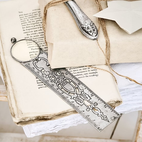 Metalllineal mit dekorativem Muster und Lupe auf alten Büchern und Vintage-Papieren