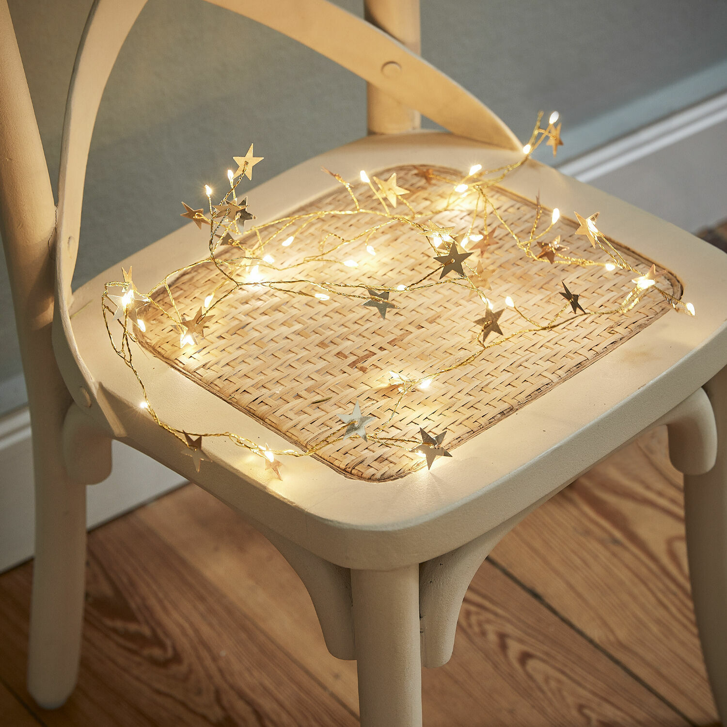 Feine Lichterkette mit Sternen in warmem Licht auf hellem Korbsitz eines Stuhls