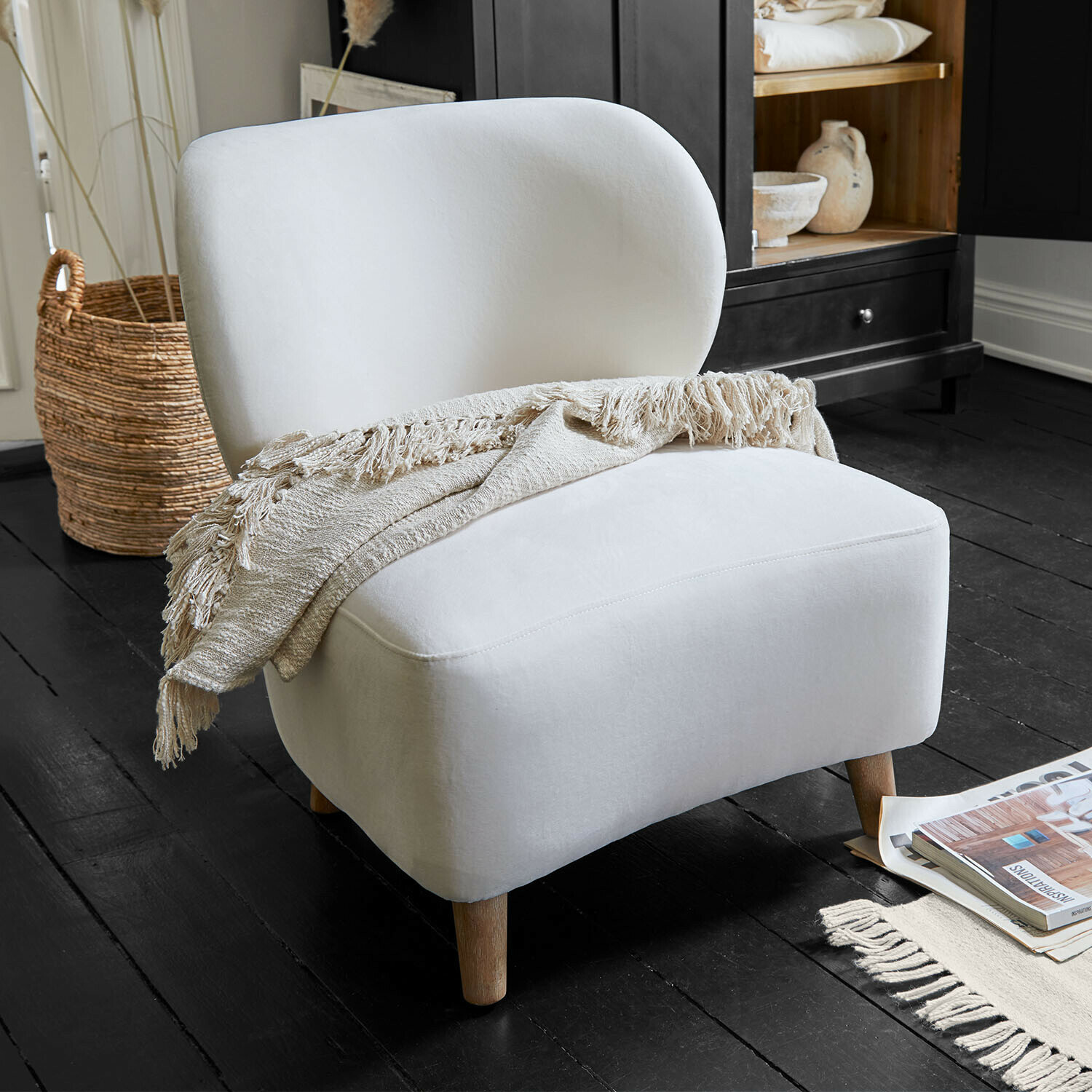 Weißer gepolsterter Sessel mit Holzbeinen und beiger Decke auf schwarzem Holzboden im Wohnzimmer