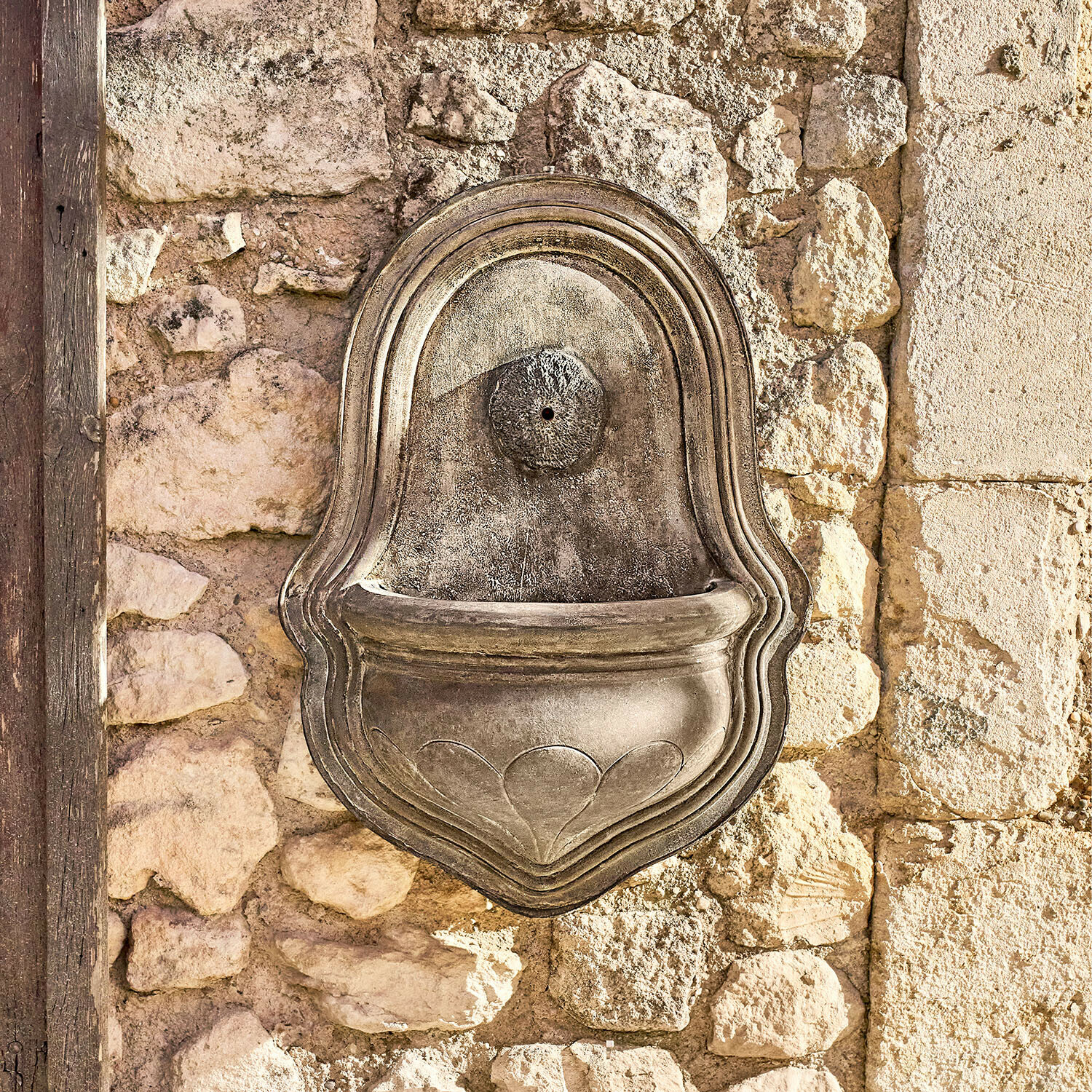 Dekorativer Wandbrunnen aus grauem Stein an einer rustikalen Steinmauer, Gartendekoration