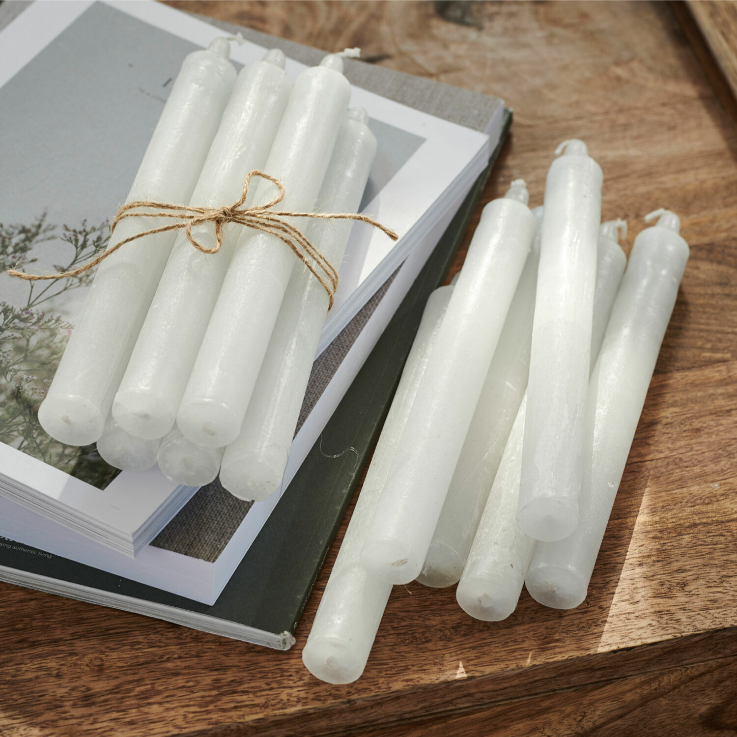 Kerze 12er Set Bauceau Set aus weißen Stabkerzen aus Wachs auf Holztisch mit Büchern, Wohnaccessoire