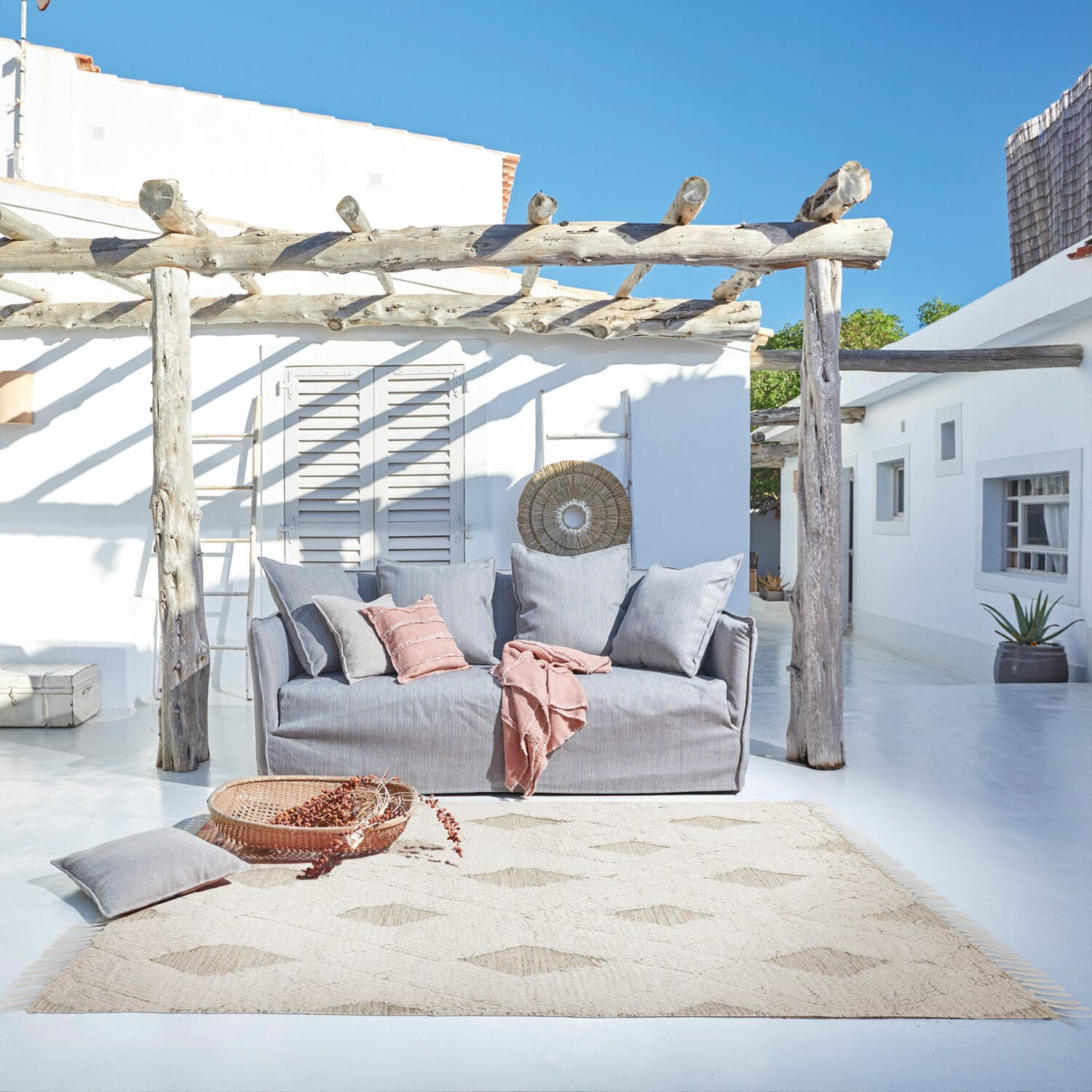 In- & Outdoor-Teppich Meagan Graues Stoffsofa auf Terrasse mit Naturteppich und rosa Kissen für entspannte Außenbereiche