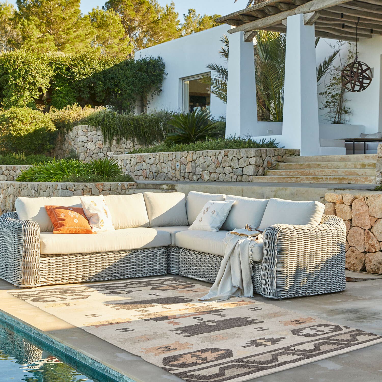 Eck-Gartensofa mit hellem Korbgeflecht und cremefarbenen Polstern auf Terrasse am Pool