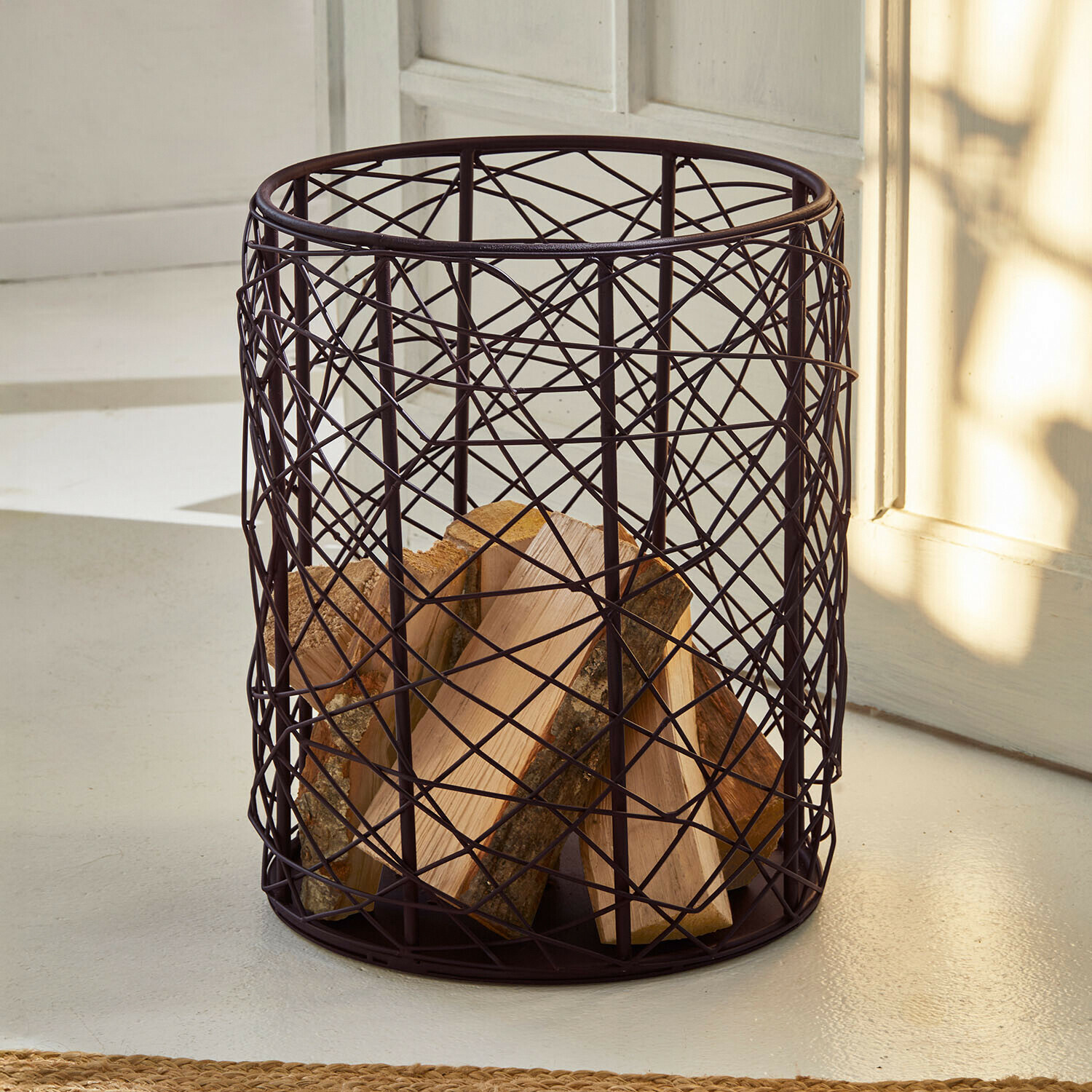 Runder Holzkorb aus dunklem Metallgitter zur Aufbewahrung von Kaminholz im Wohnraum