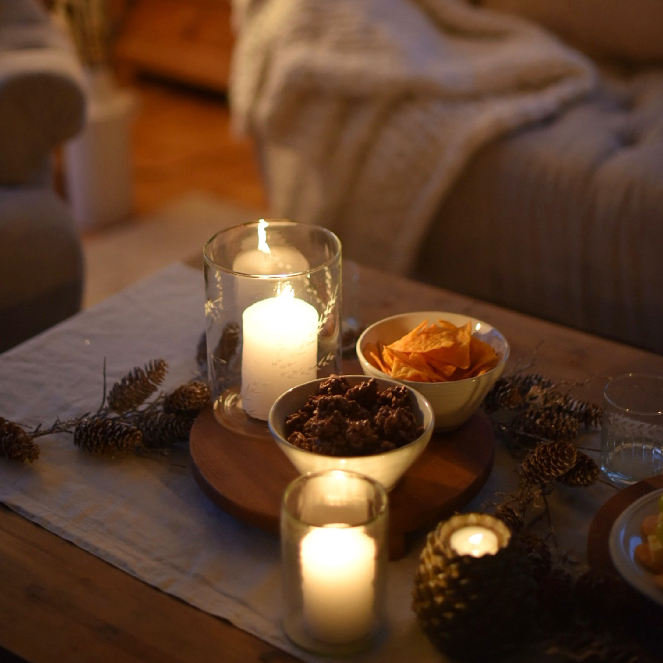 Kerzen in Glaswindlichtern und Schalen mit Snacks auf Holztisch in gemütlicher Wohnatmosphäre