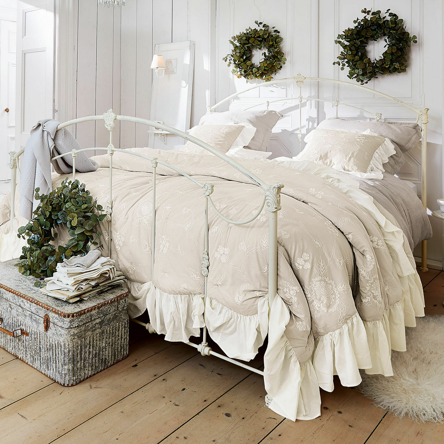 Quilt Clarissa Beige bestickte Bettwäsche mit Rüschen auf weißem Metallbett in hellem Schlafzimmer mit grünen Kränzen