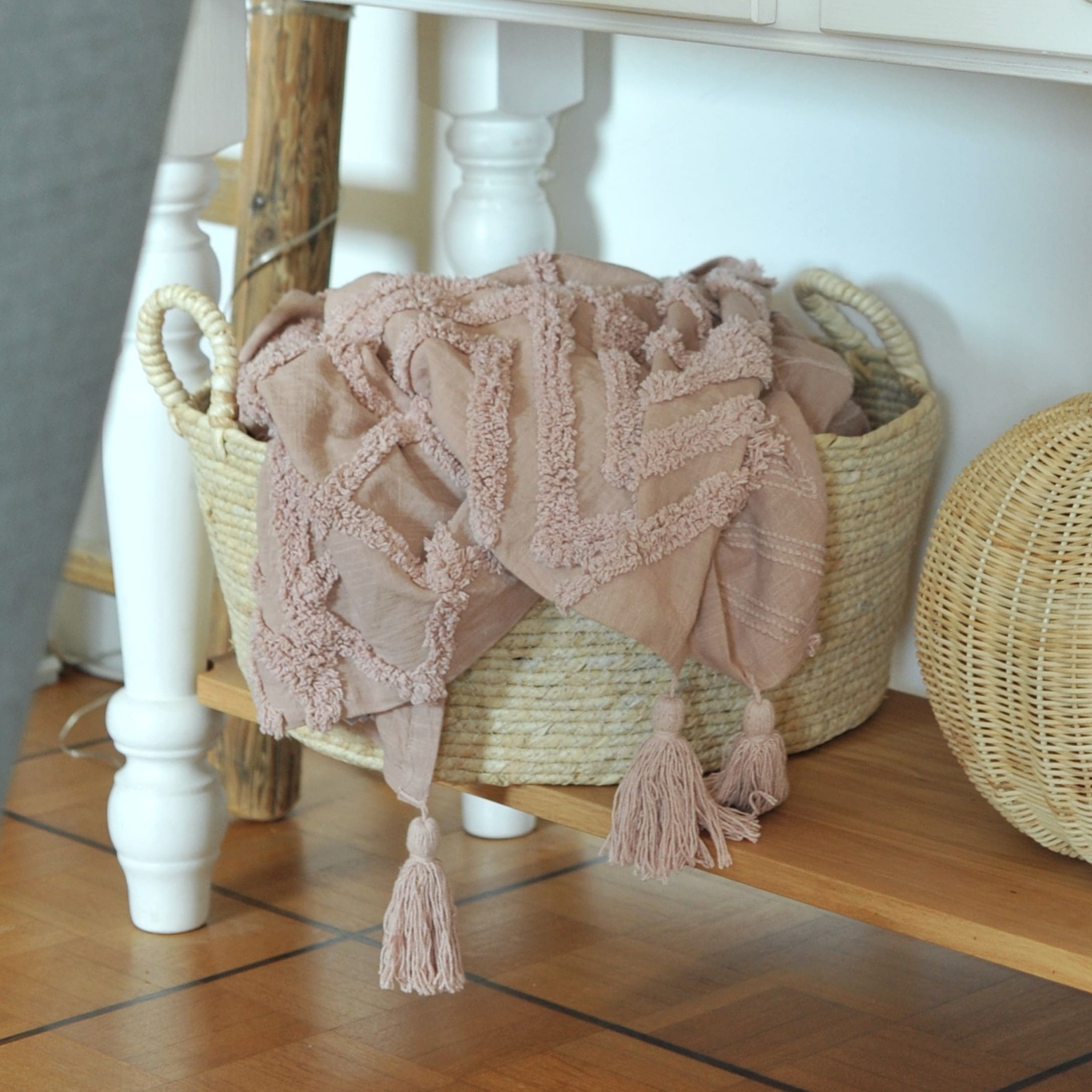 Rosa dekorative Decke mit Quasten im Korb aus Weide auf Holzregal in hellem Raum
