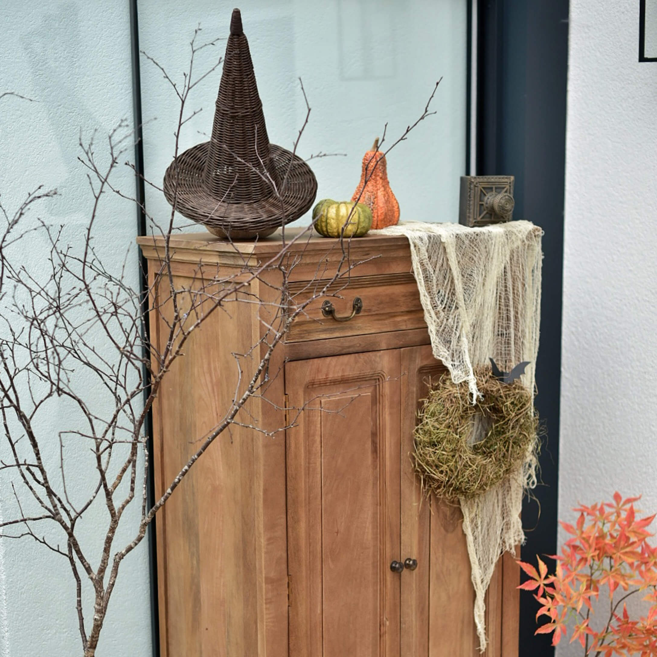 Holzschrank mit herbstlicher Dekoration: geflochtener Hut, Kürbisse und Mooskranz