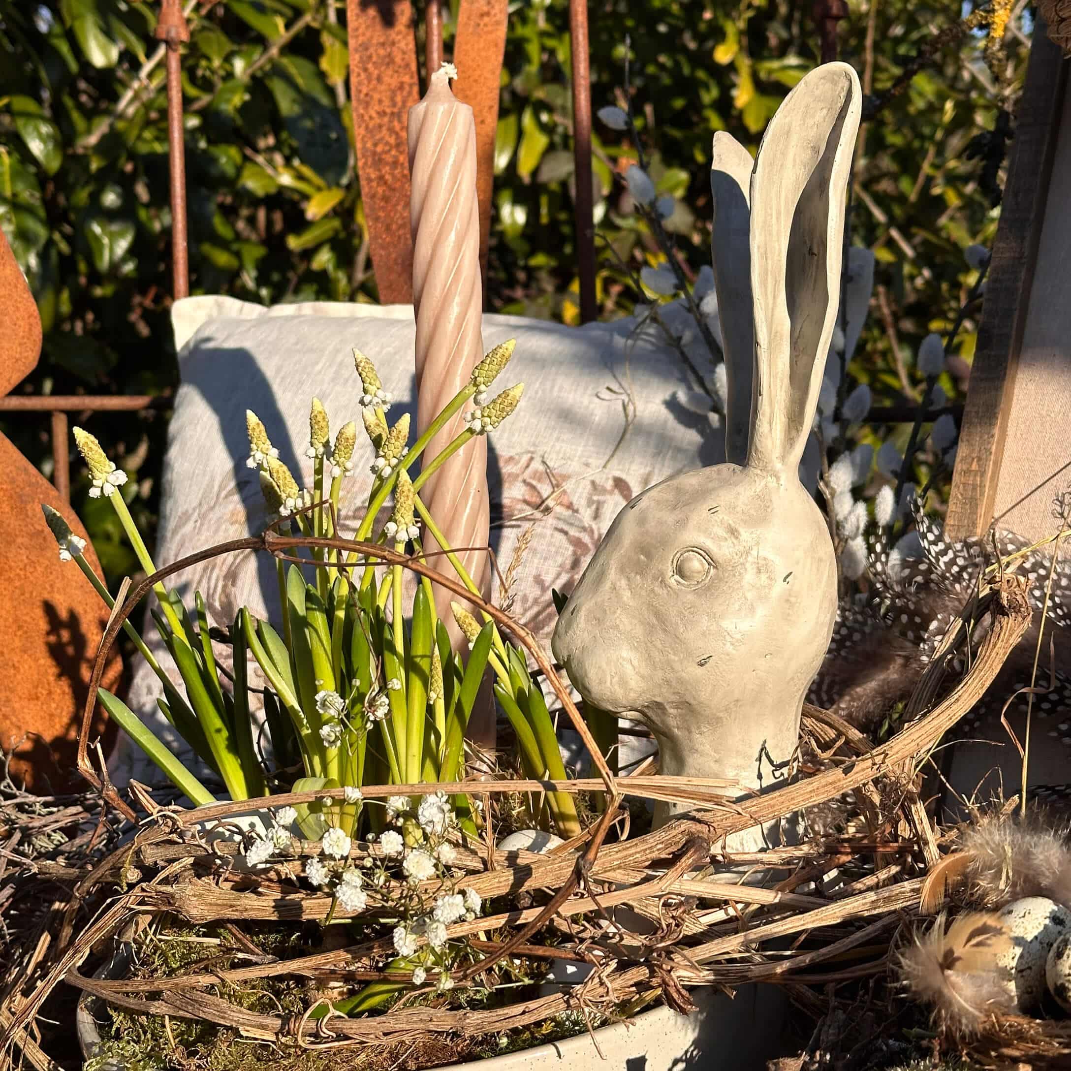 Natürlich dekorierte Osterfreude mit grauem Keramikhasenkopf und grünen Blumen im Naturkorb