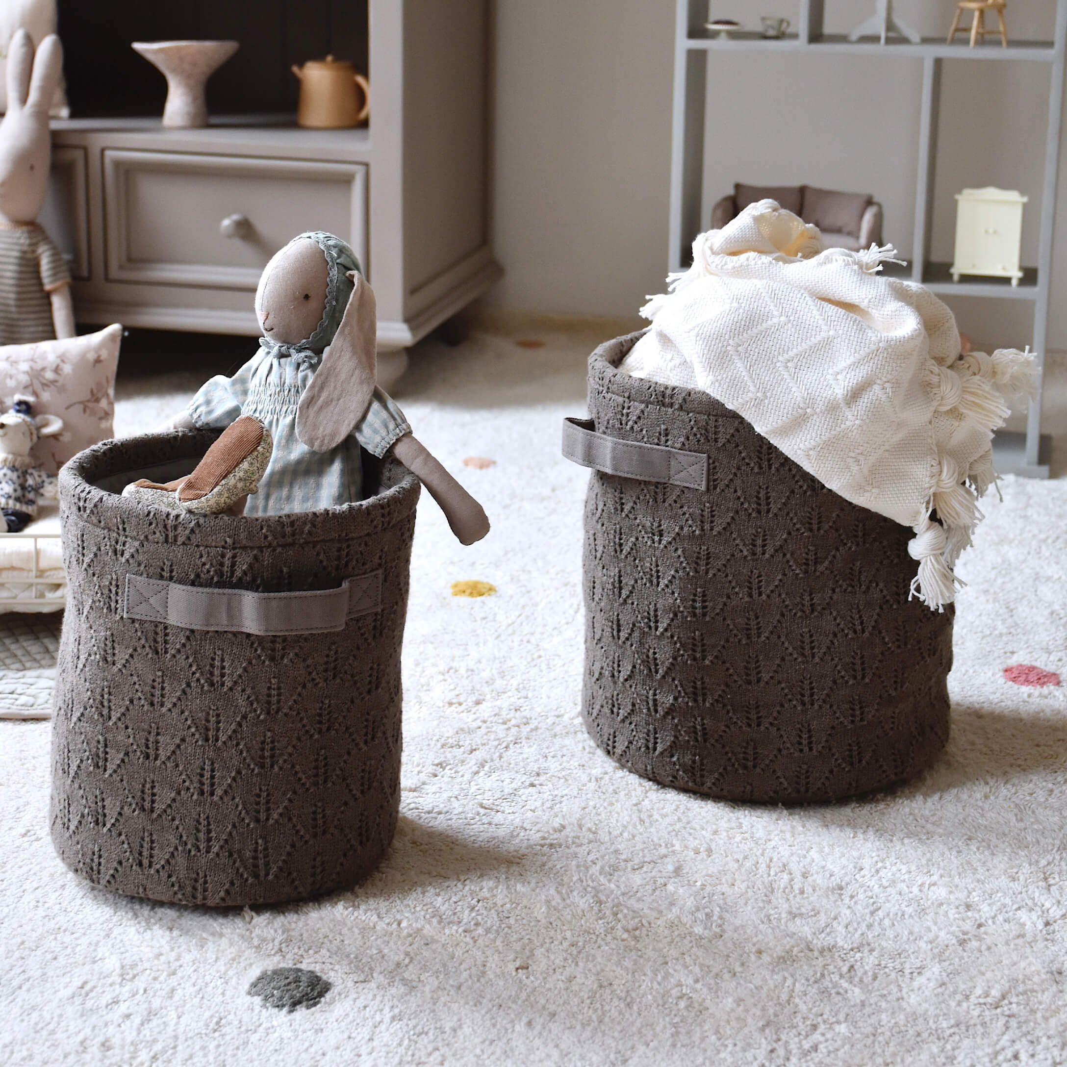 Braune gestrickte Aufbewahrungskörbe mit Griffen, gefüllt mit Spielzeug und Decke auf hellem Teppich